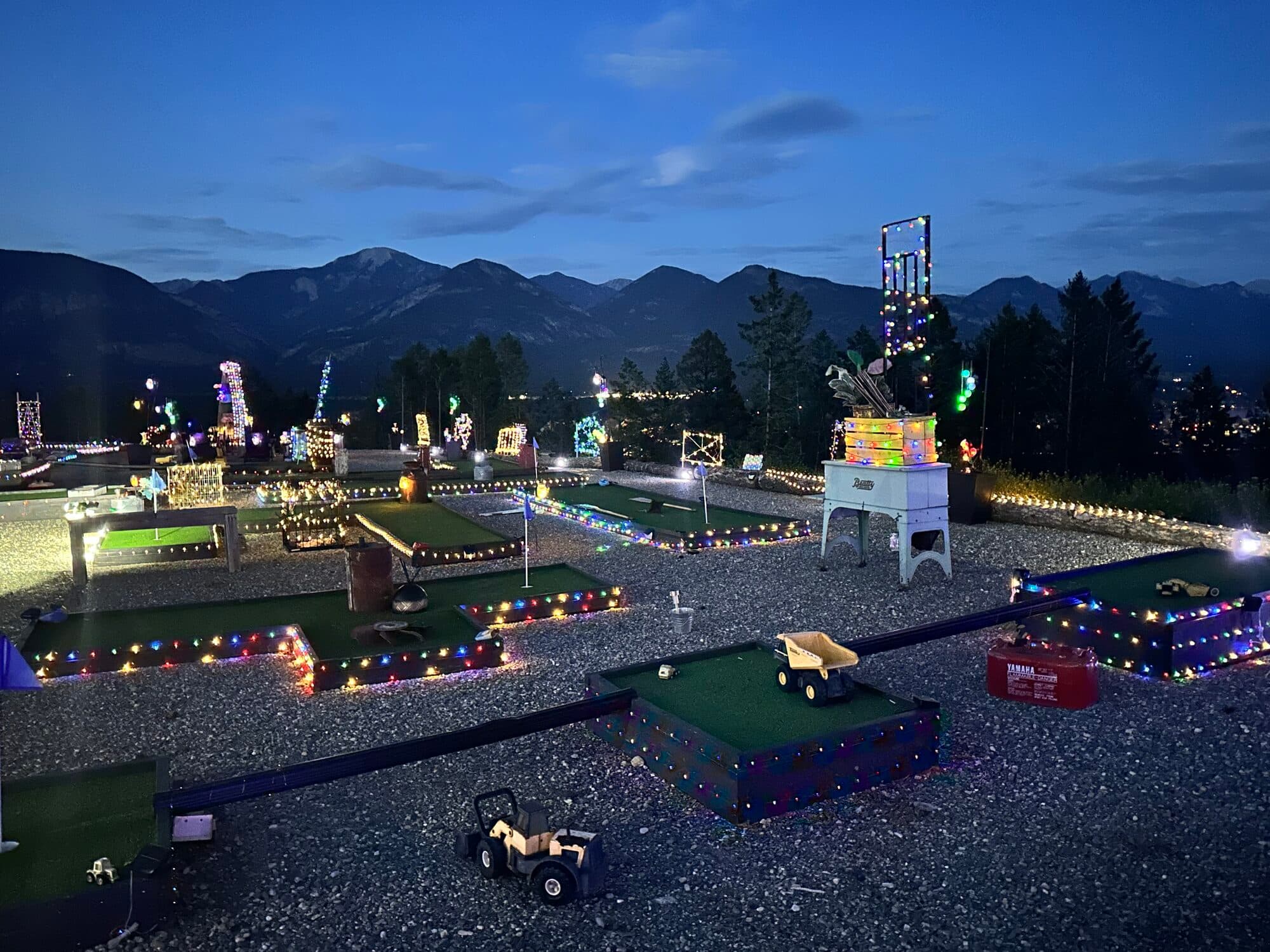 Reimagine Ranch outdoor area lit up at dusk — mini golf, lights and mountain backdrop