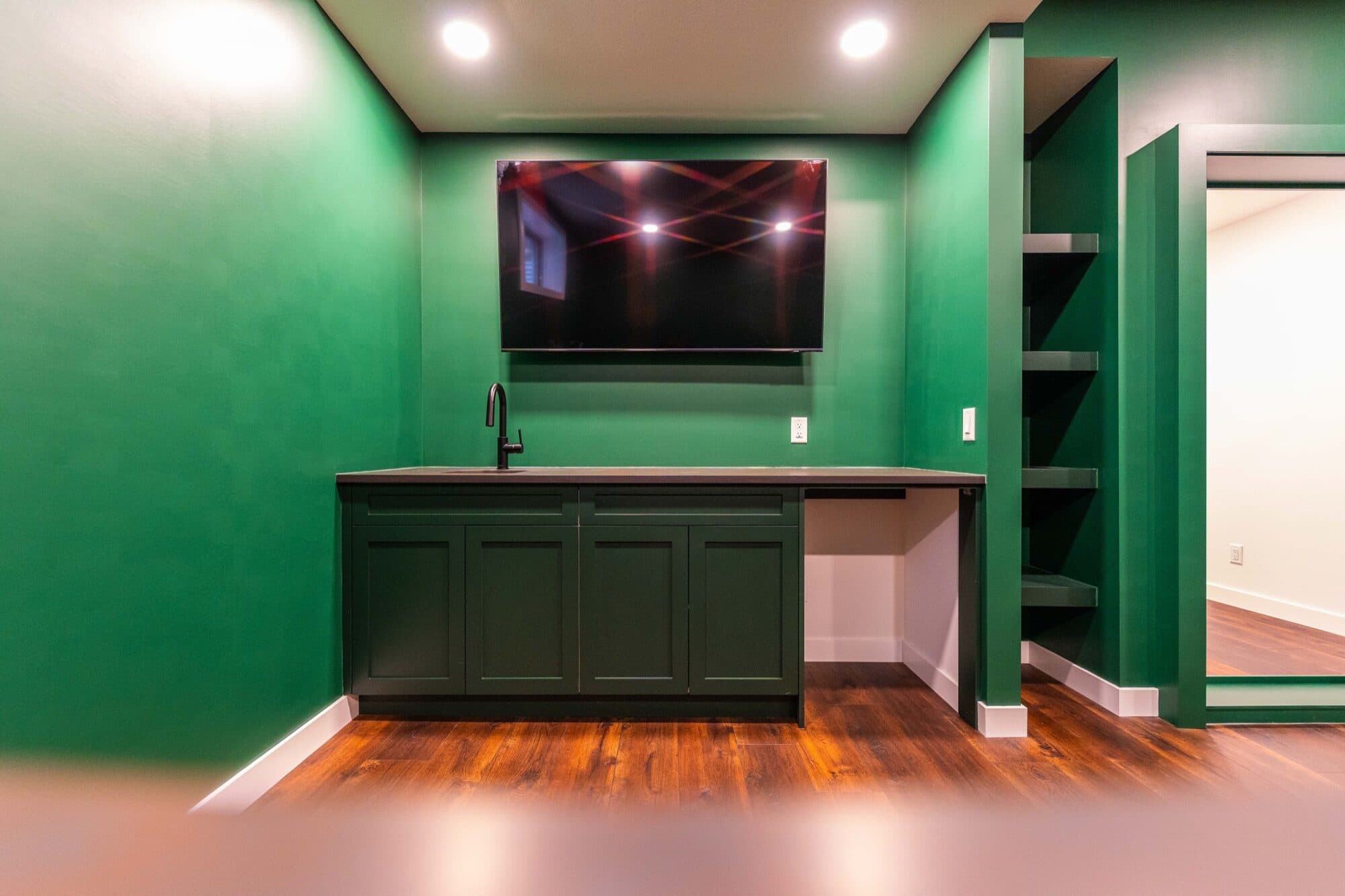 Basement flex room with an emerald-green feature wall and built-in bar cabinetry