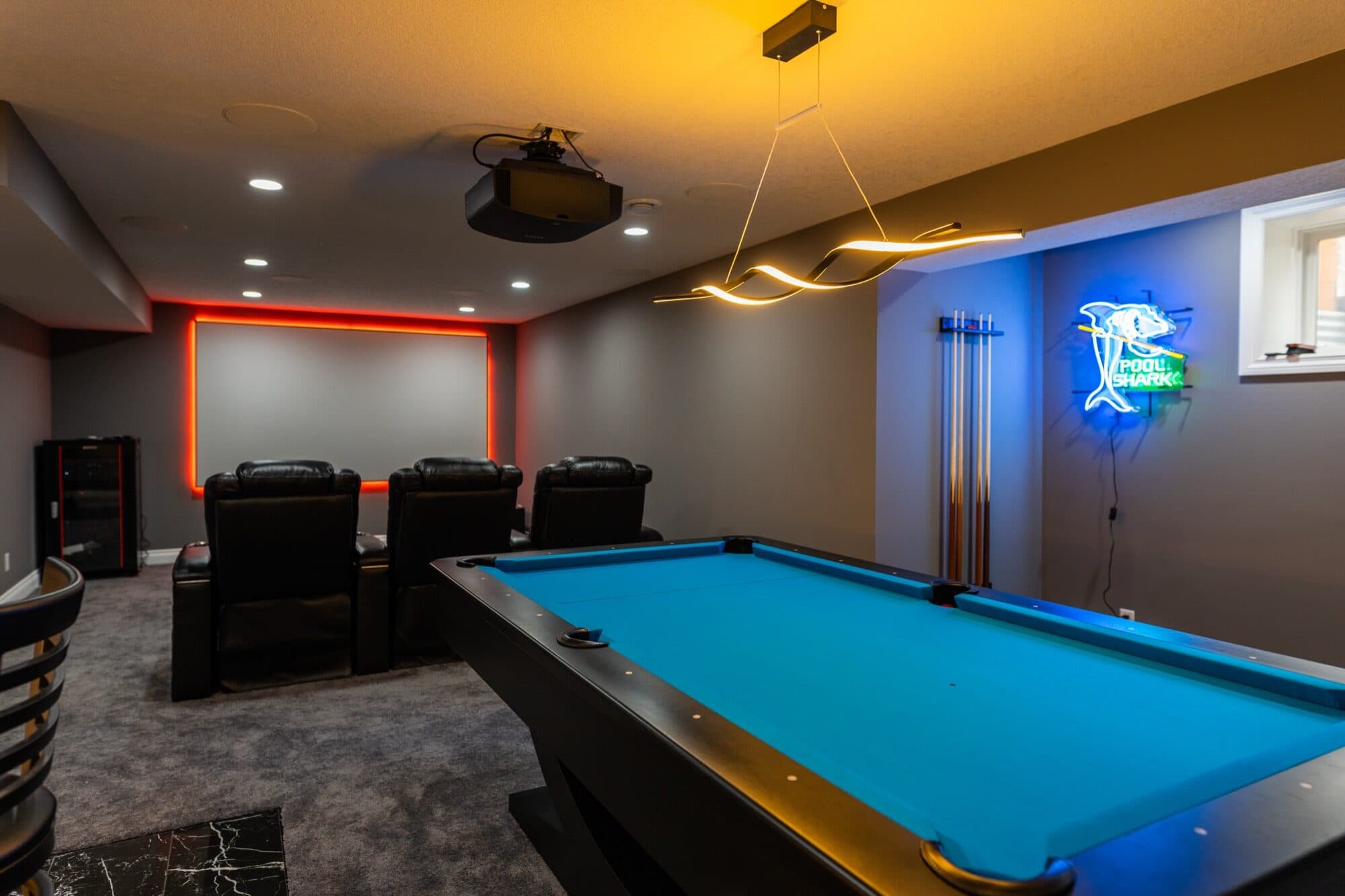 Basement games lounge with a billiards table, neon accents and theatre seating