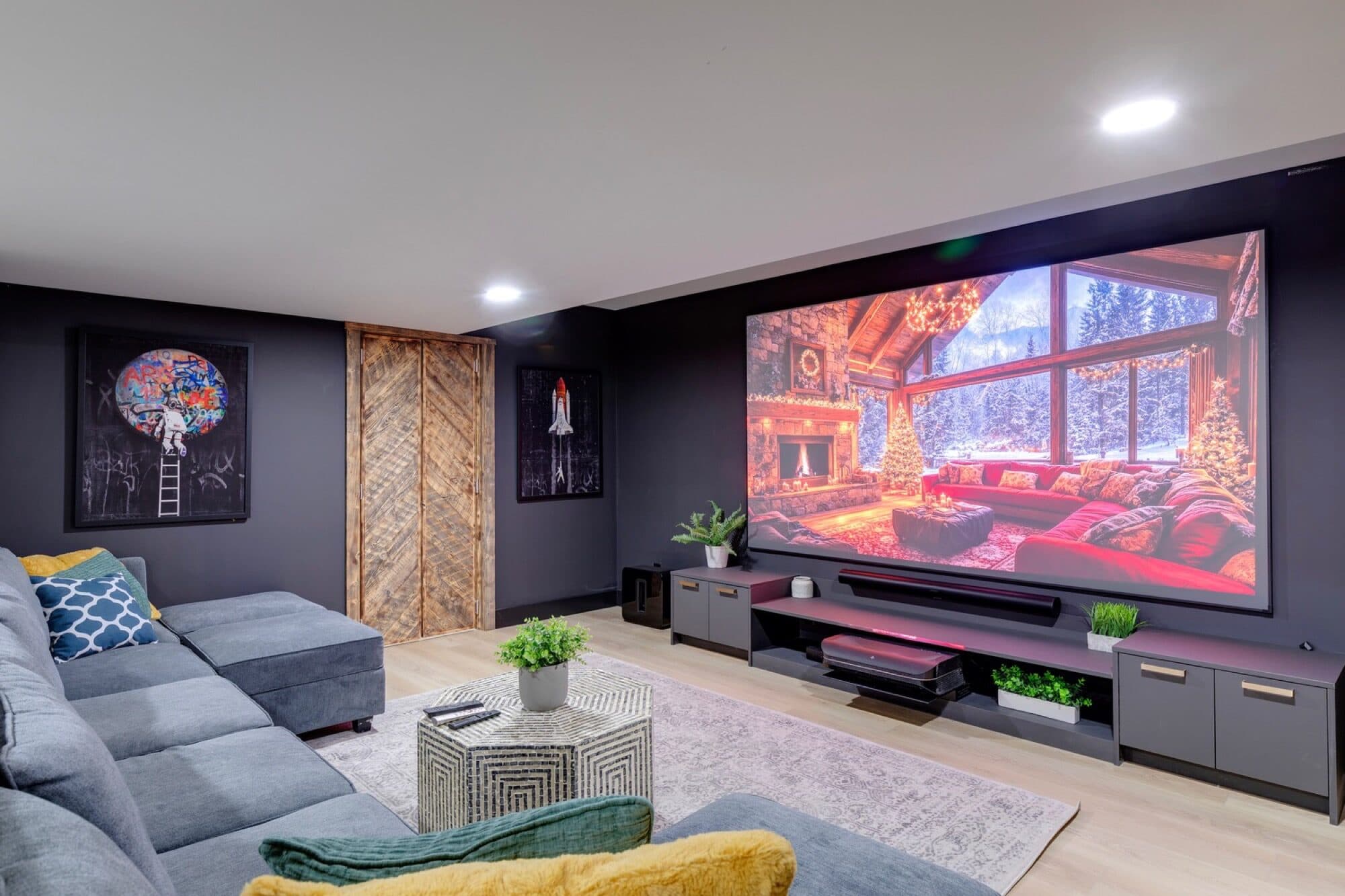 Basement media lounge with grey sectional and large cabin-scene screen