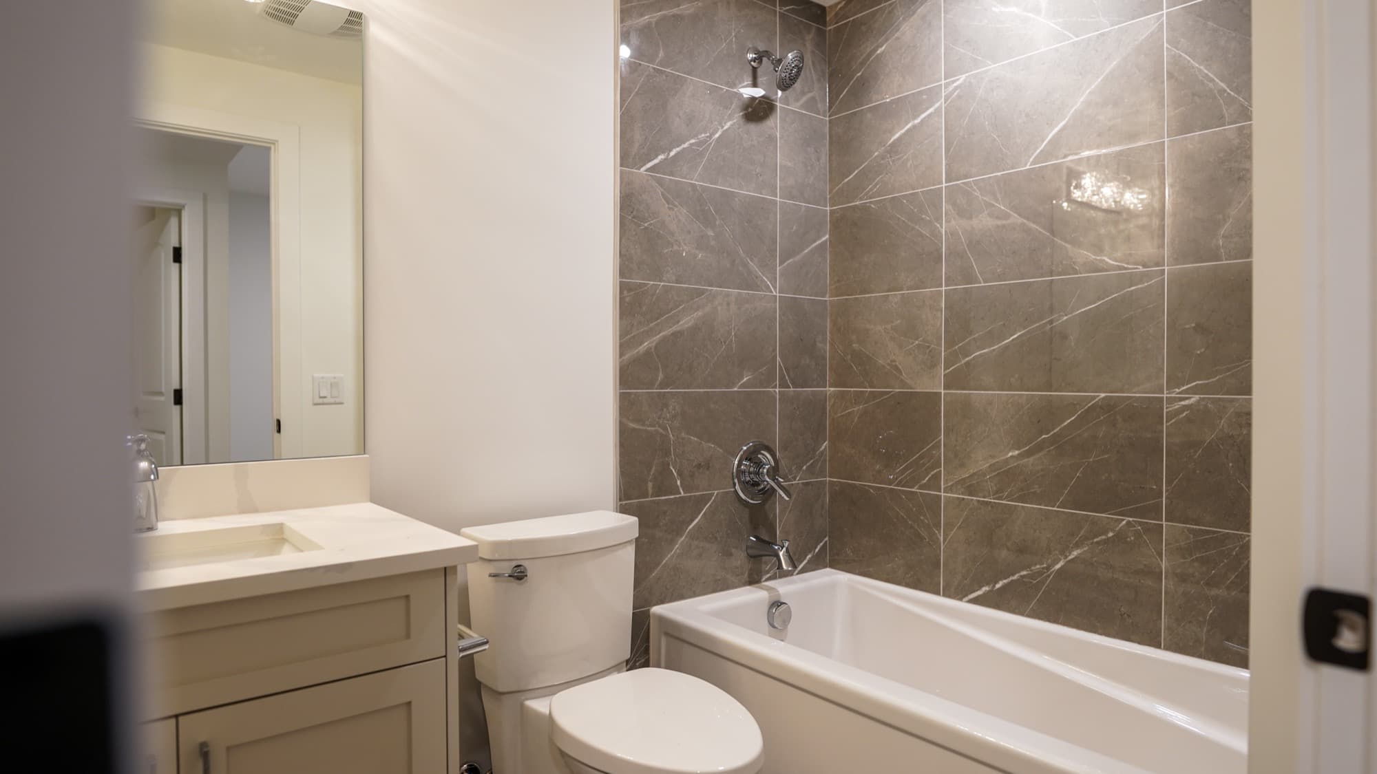 Basement bathroom with grey marble tub-shower tile, quartz vanity and toilet