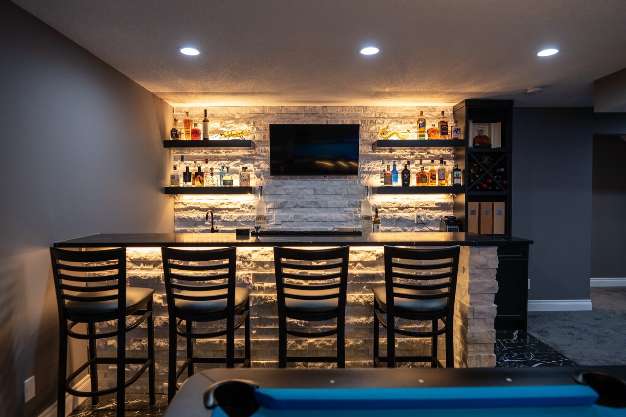 Full wet bar with warm-lit liquor shelves, bar stools and pool table