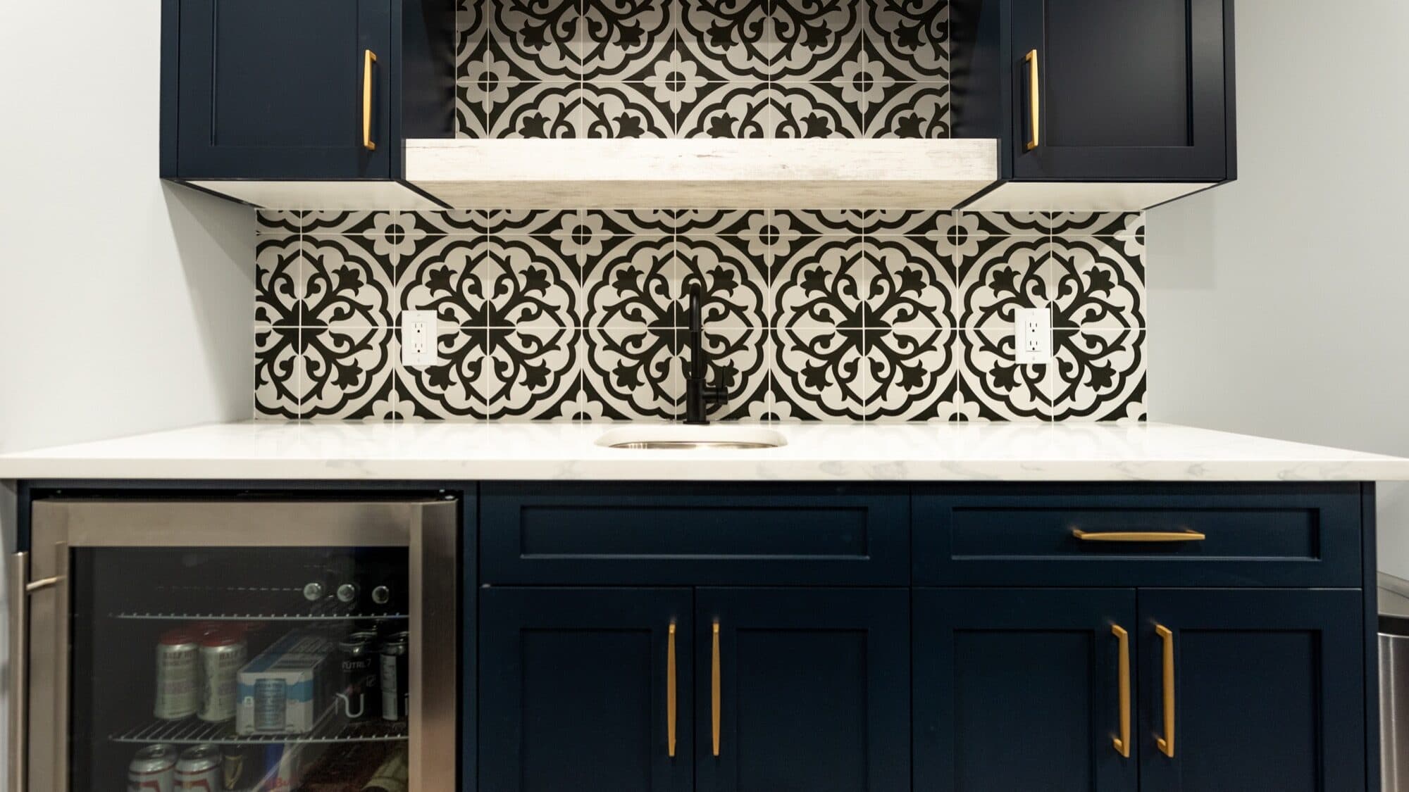 Navy basement bar with patterned tile backsplash and gold hardware