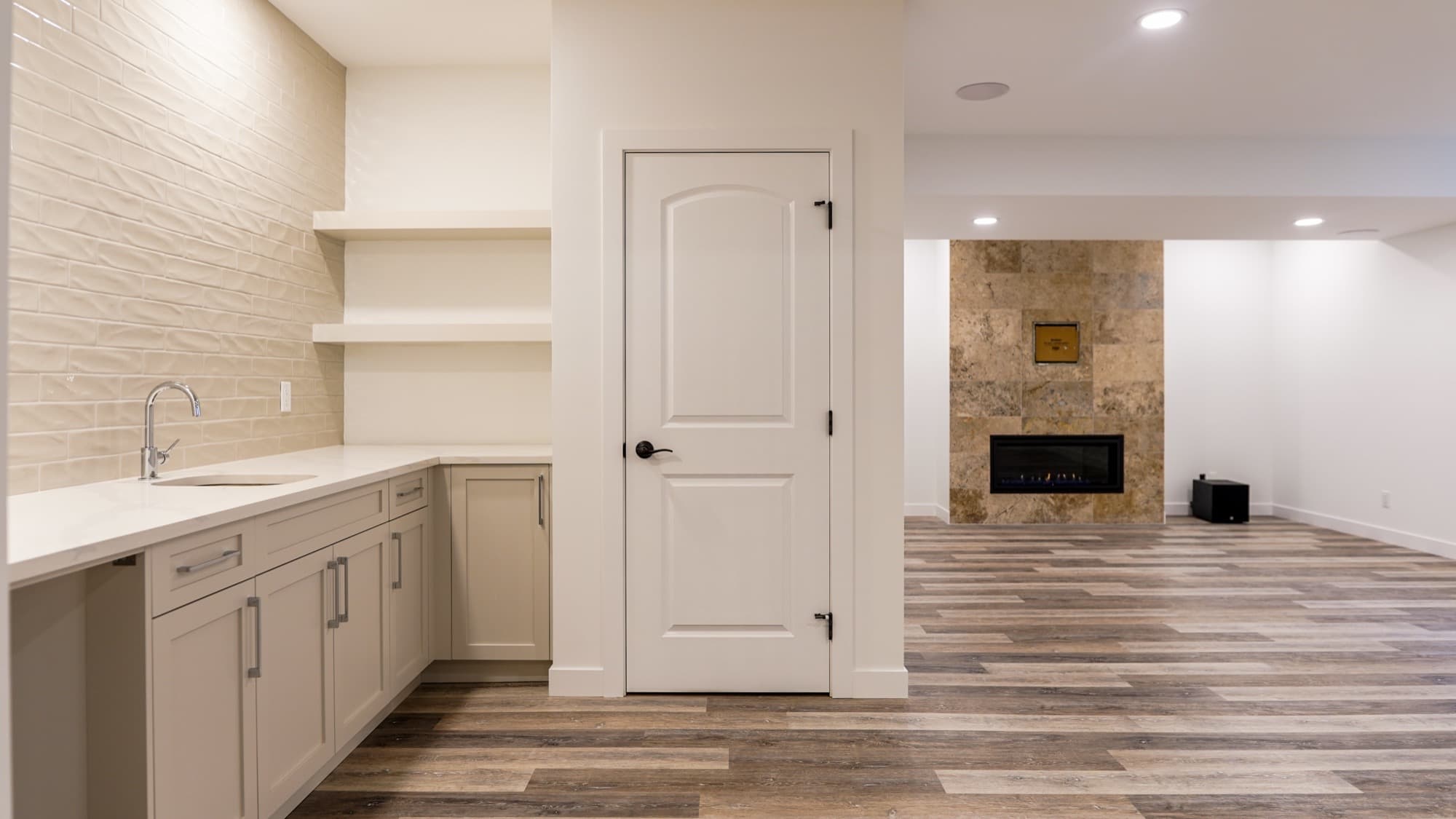 Open-plan basement with built-in bar area and stone fireplace wall