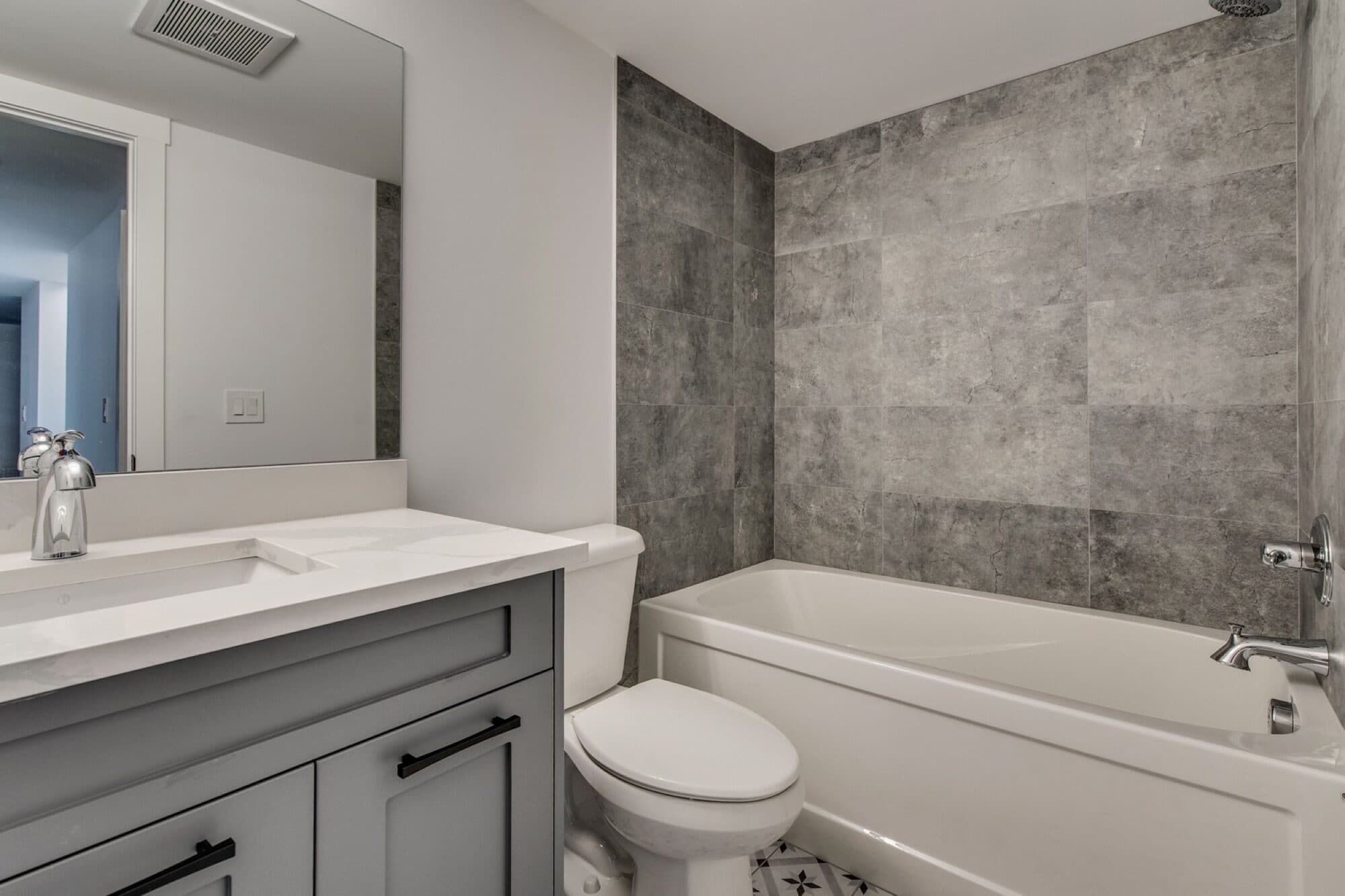 Basement bathroom with grey tile tub surround and quartz vanity