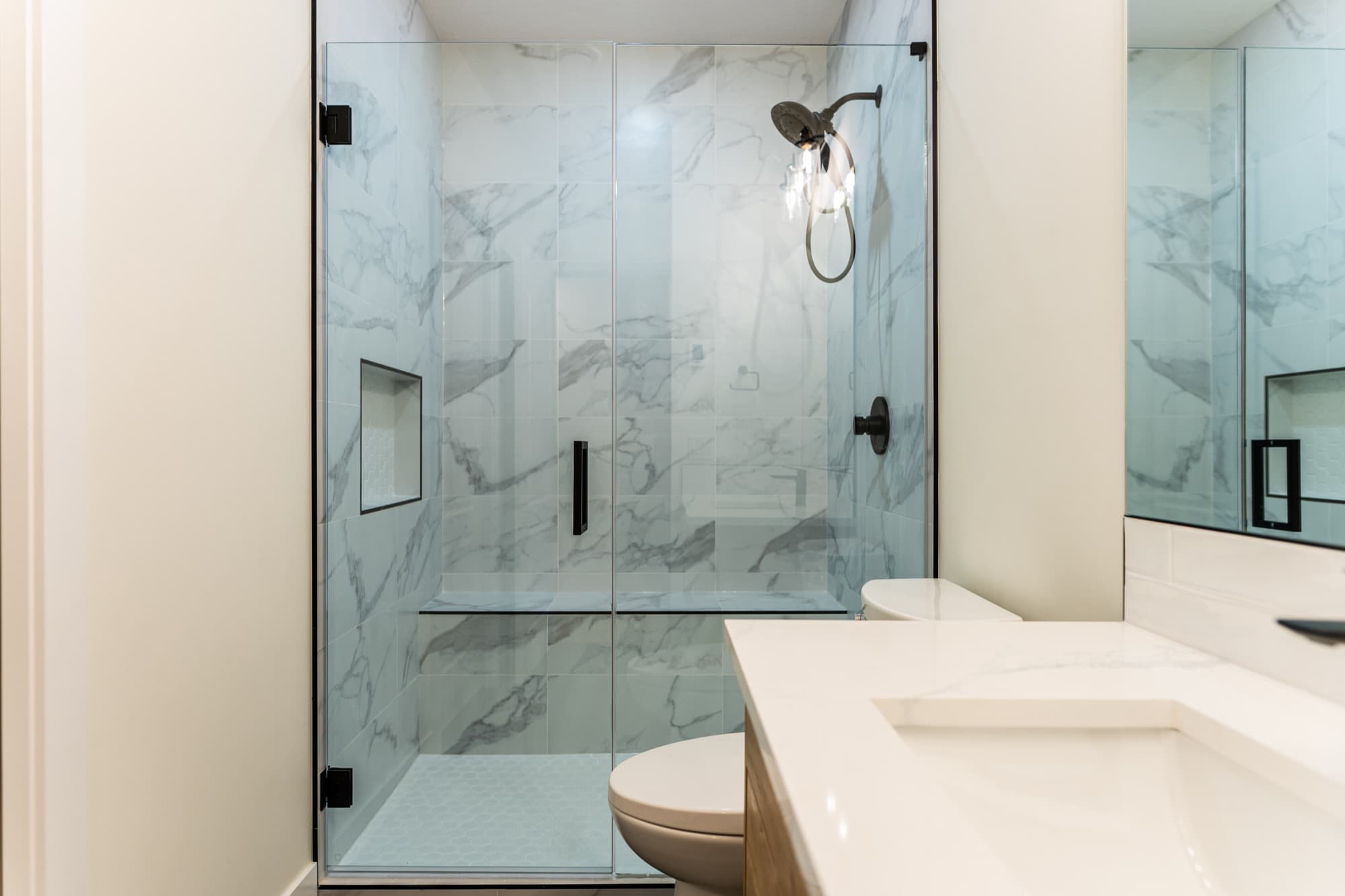 Frameless glass shower with large marble-look tile and black hardware