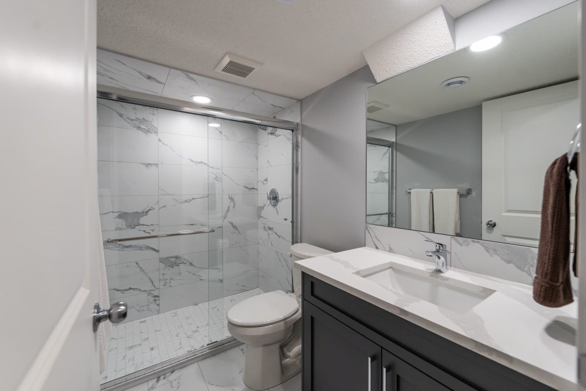 Marble-tile basement bathroom with sliding glass shower and double vanity