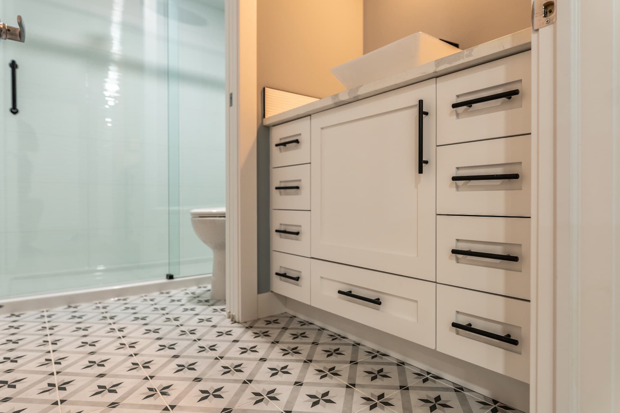 Basement bathroom with patterned floor tile, glass shower and white vanity