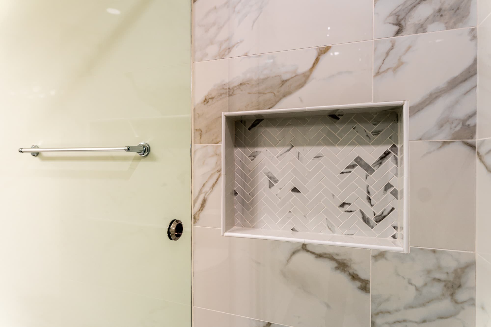 Marble shower niche detail with herringbone inset tile and glass panel