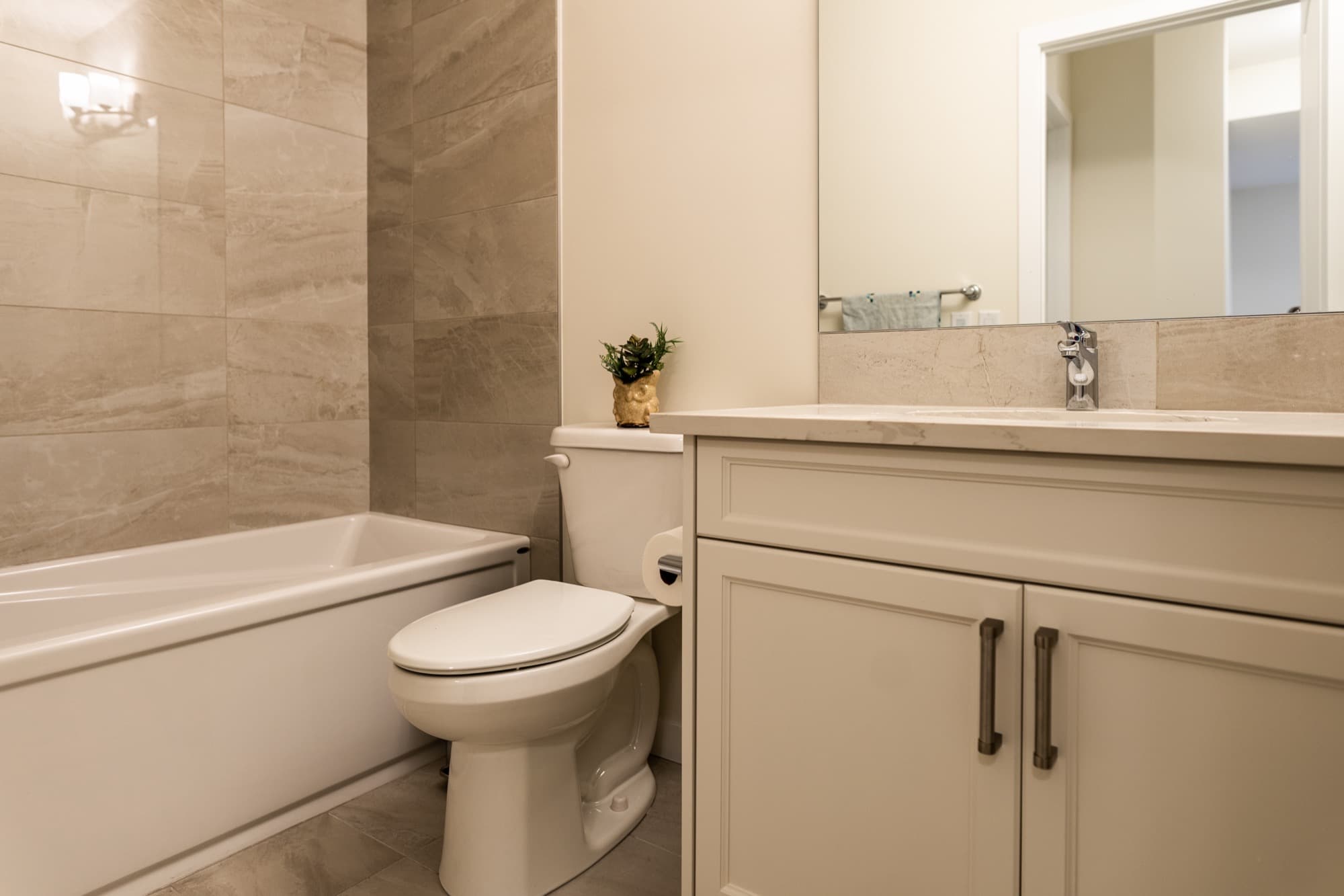 Beige basement bathroom with soaker tub, large tile and cream vanity
