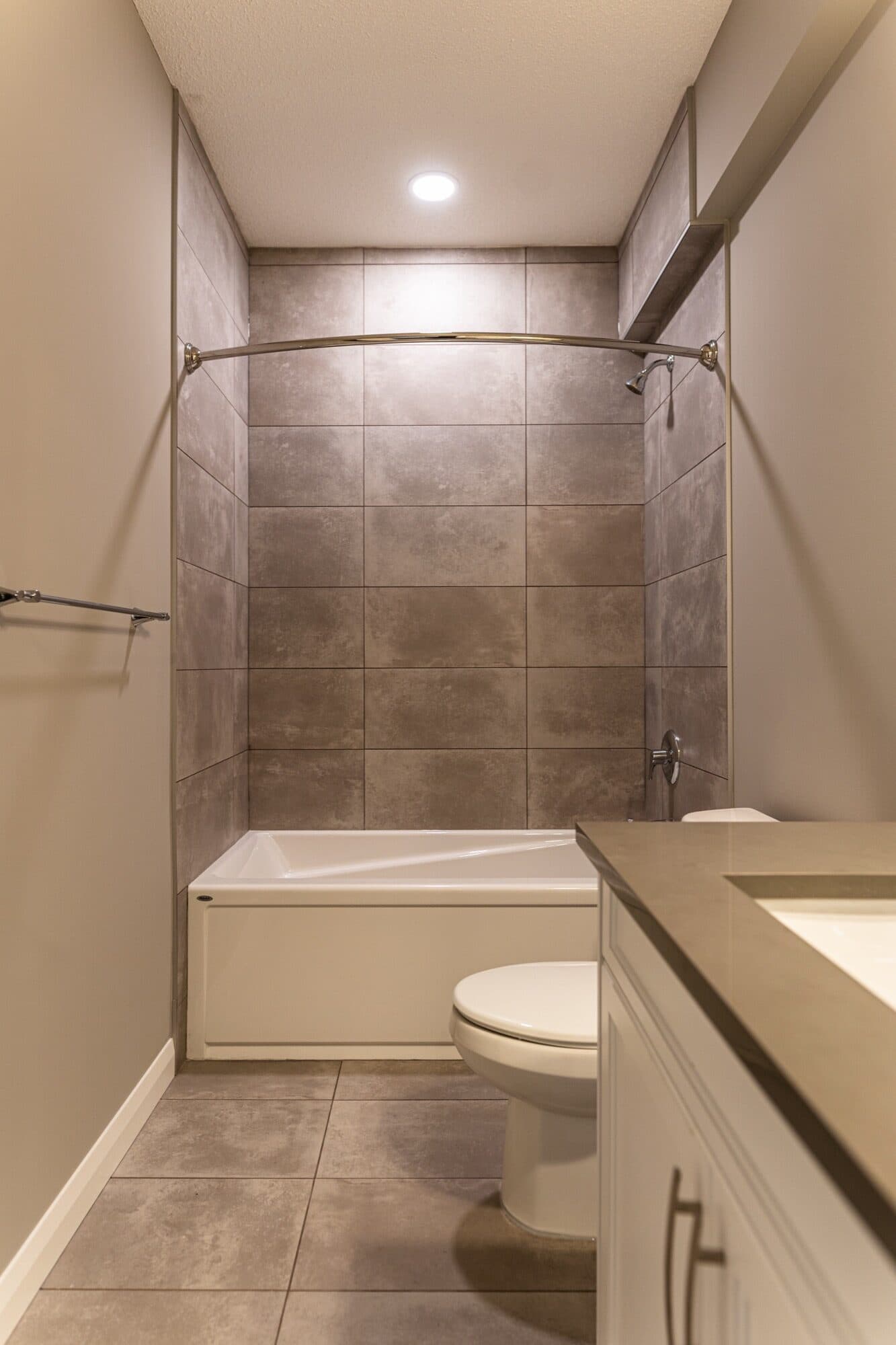 Full-room basement bathroom with tub-shower and large grey tile