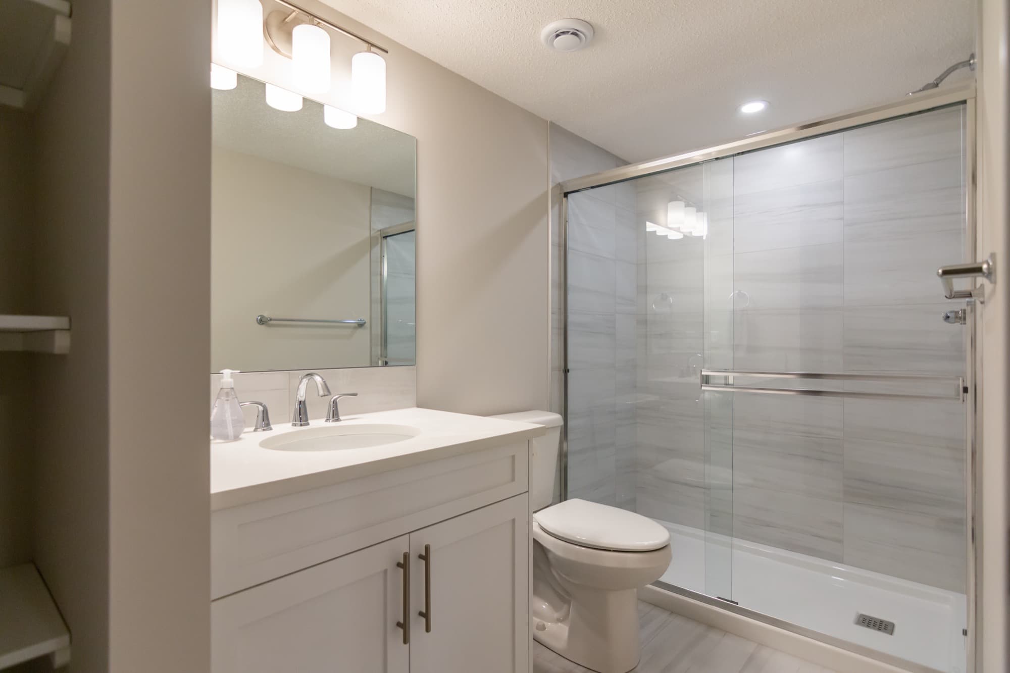 Clean white basement bathroom with glass slide shower and white vanity