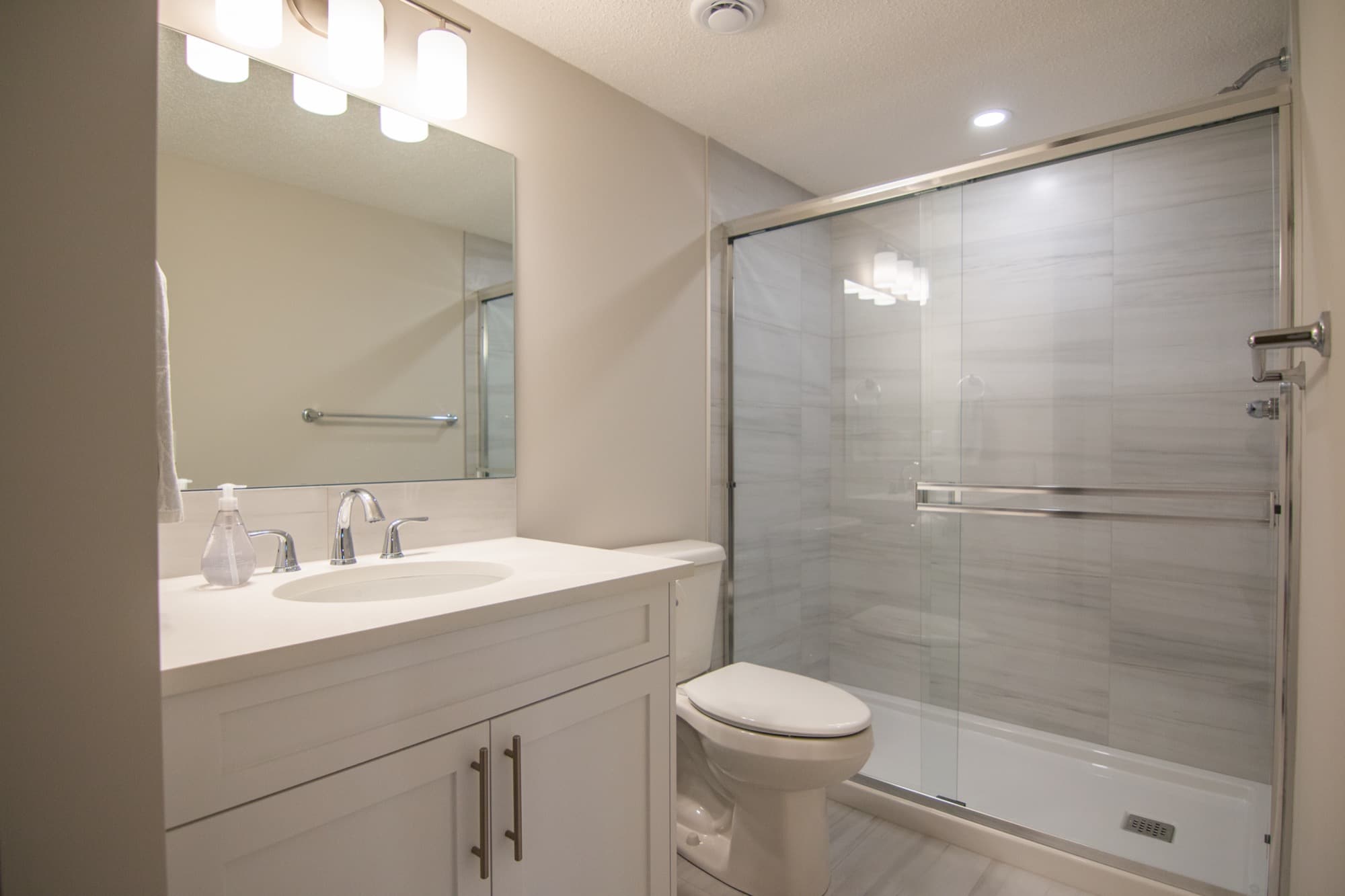 White basement bathroom with glass slider shower, alternate angle