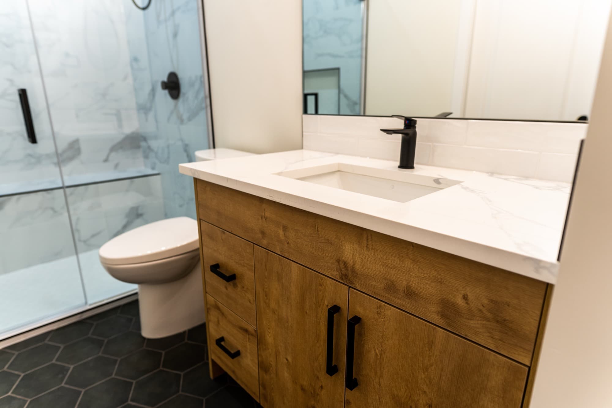 Modern basement bathroom with wood vanity, quartz top and marble shower