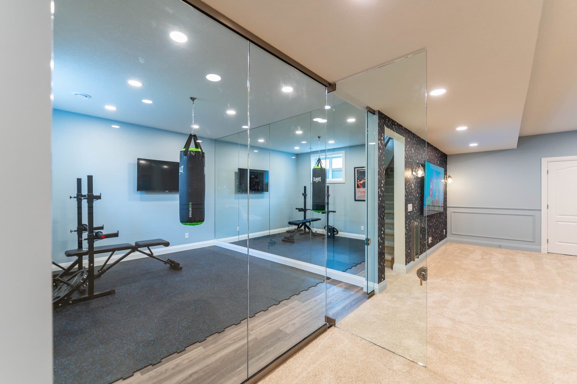 Basement glass-partition gym with boxing bag from the hallway view