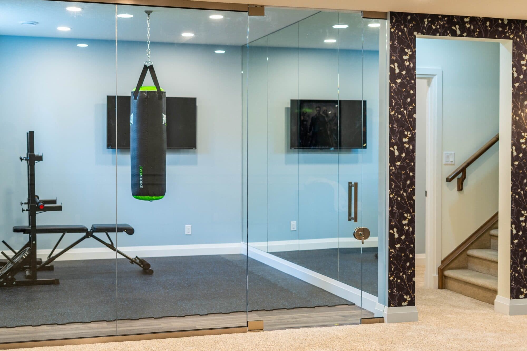 Basement gym with glass wall, boxing bag and marble accent staircase