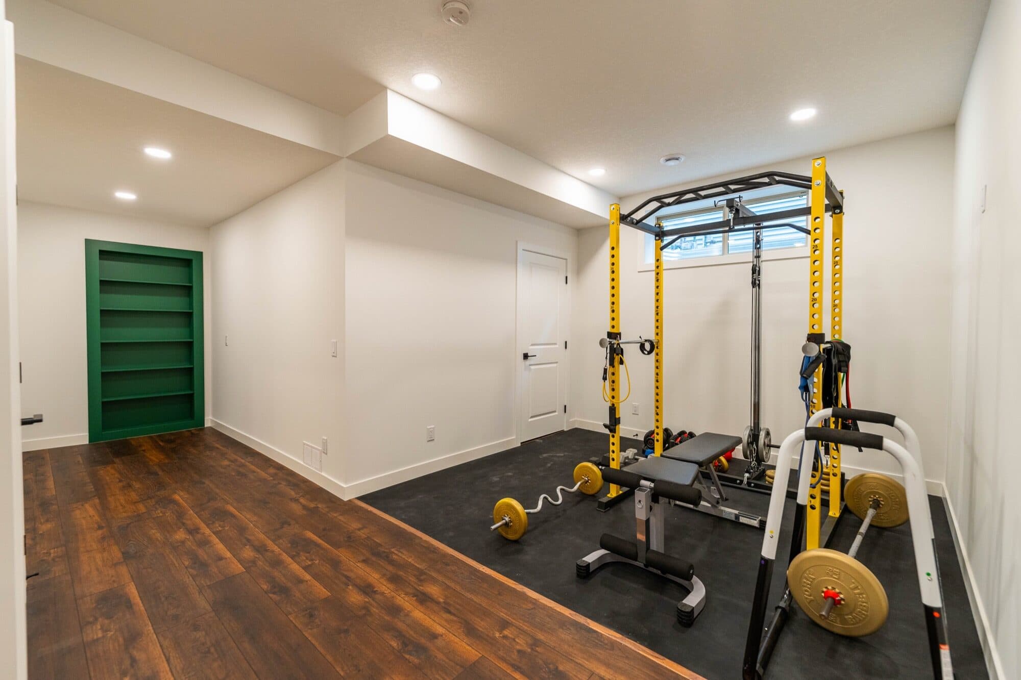 Basement gym with yellow power rack and bench on dark hardwood floors