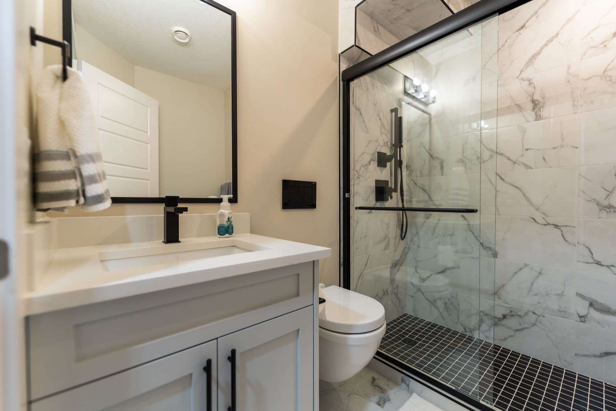 Basement bathroom with black marble glass shower and white shaker vanity