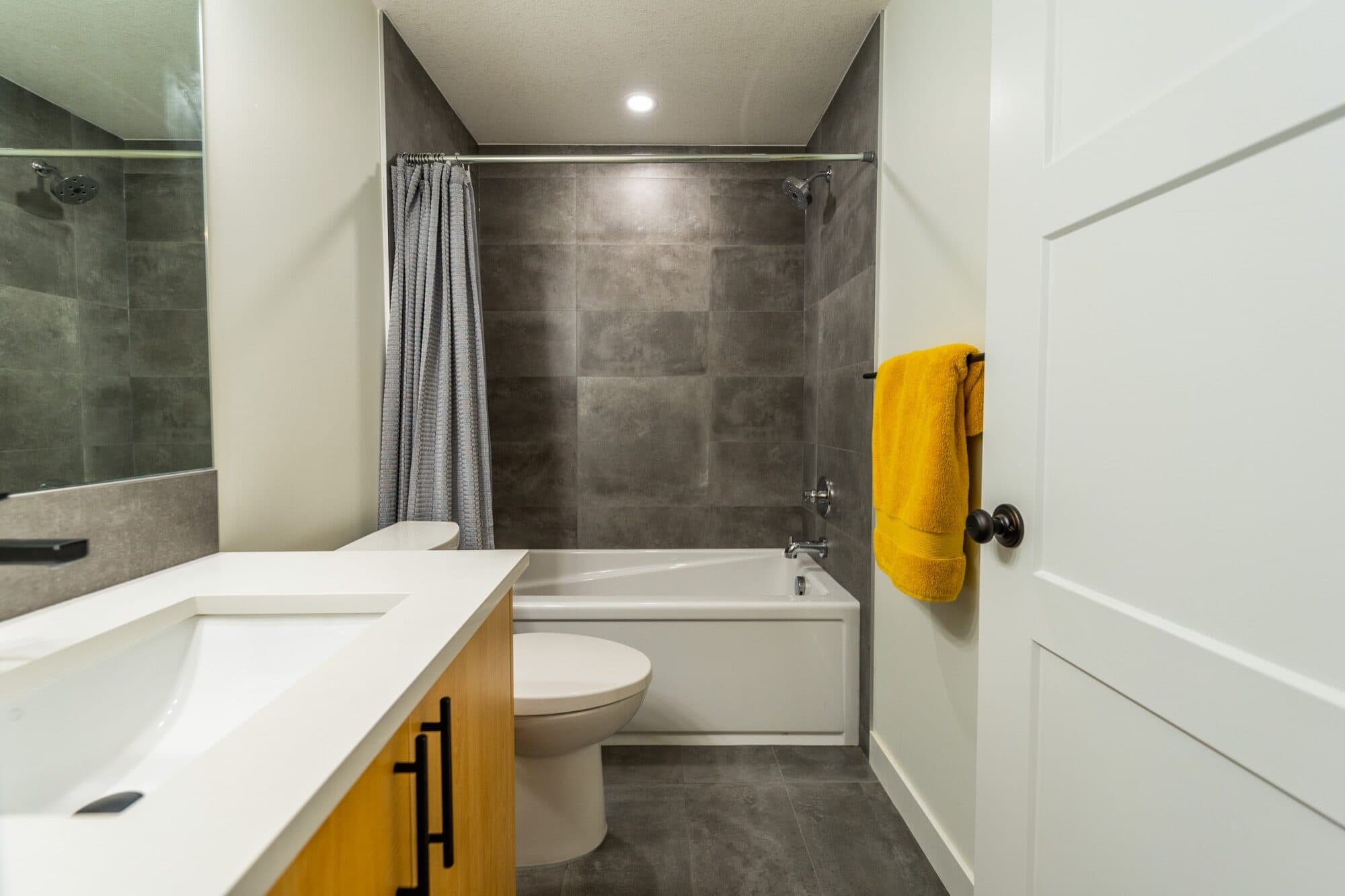 Basement bathroom with dark tile tub-shower and wood vanity