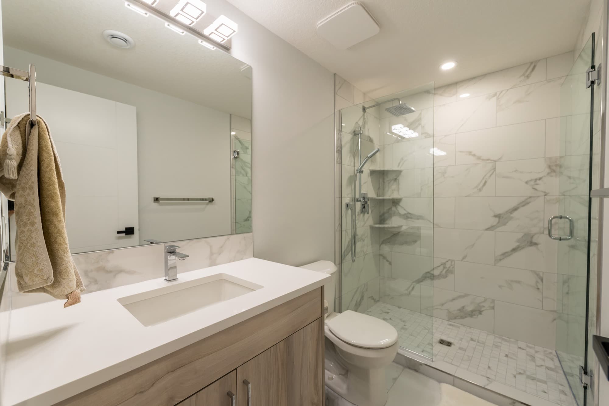 Basement bathroom with marble tile walk-in glass shower and wood vanity