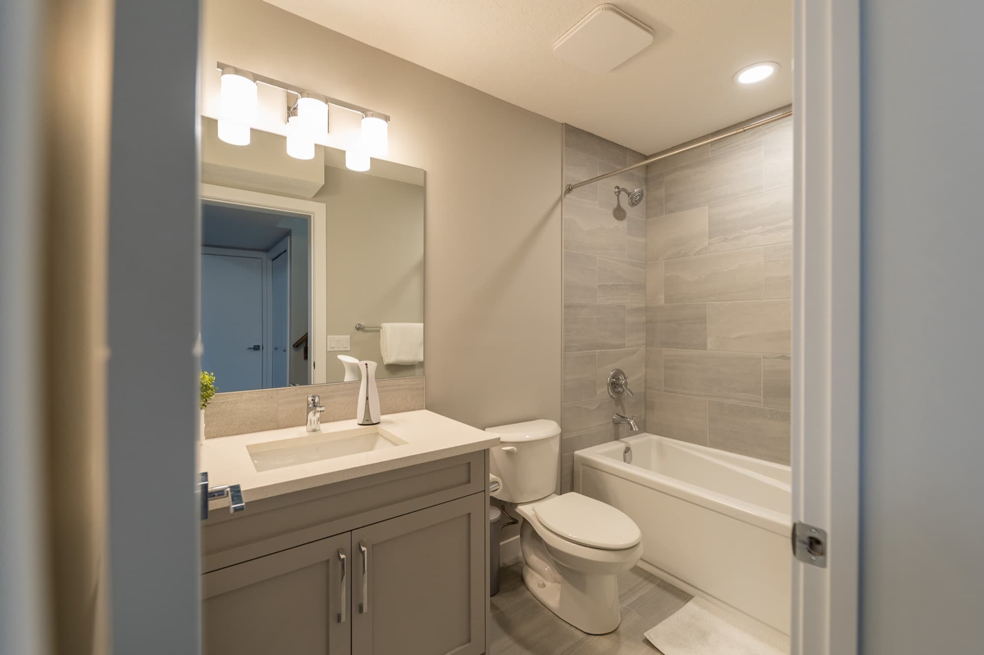 Basement bathroom with grey shaker vanity and tub-shower tile surround