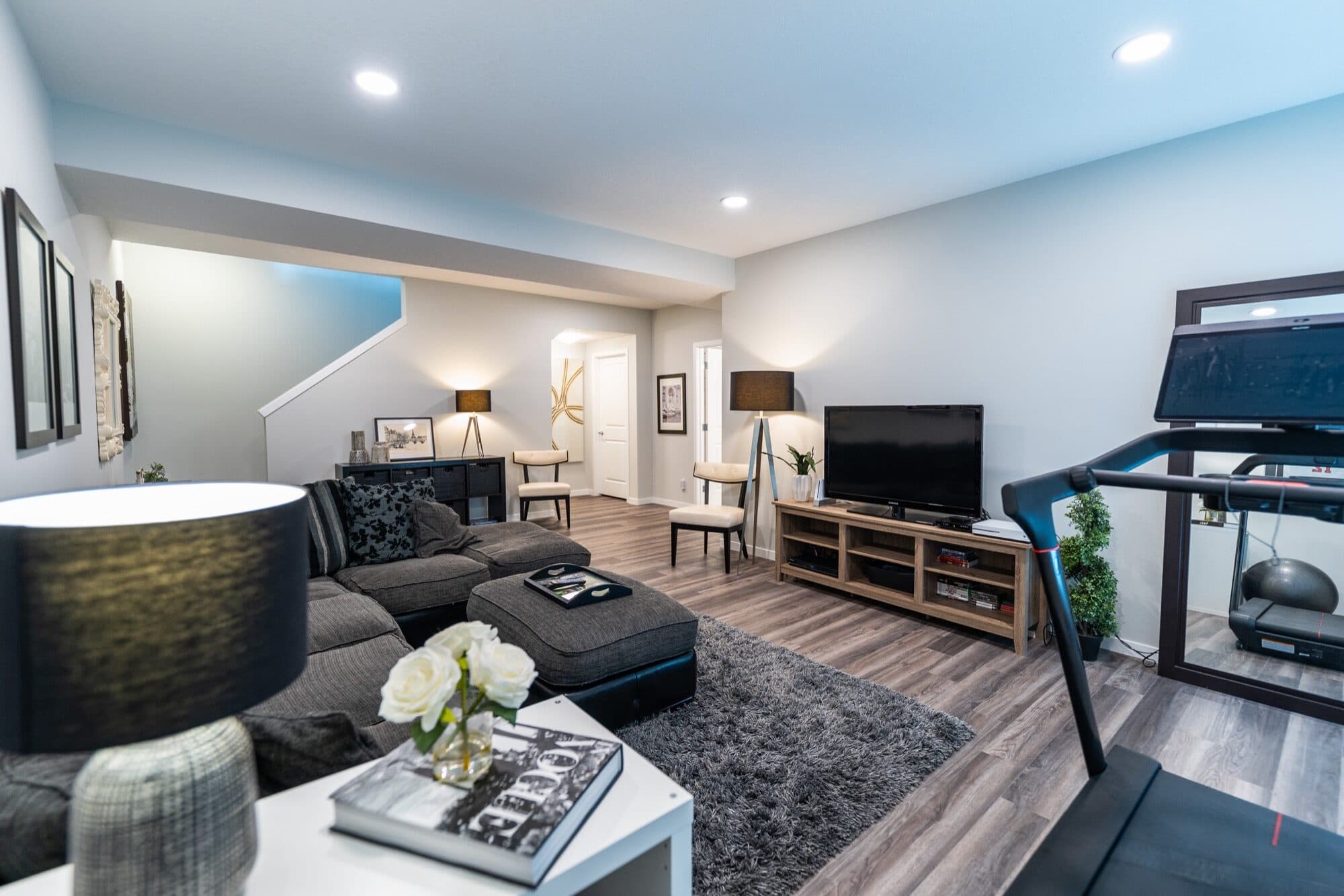 Basement rec room with sectional sofa, treadmill and open staircase