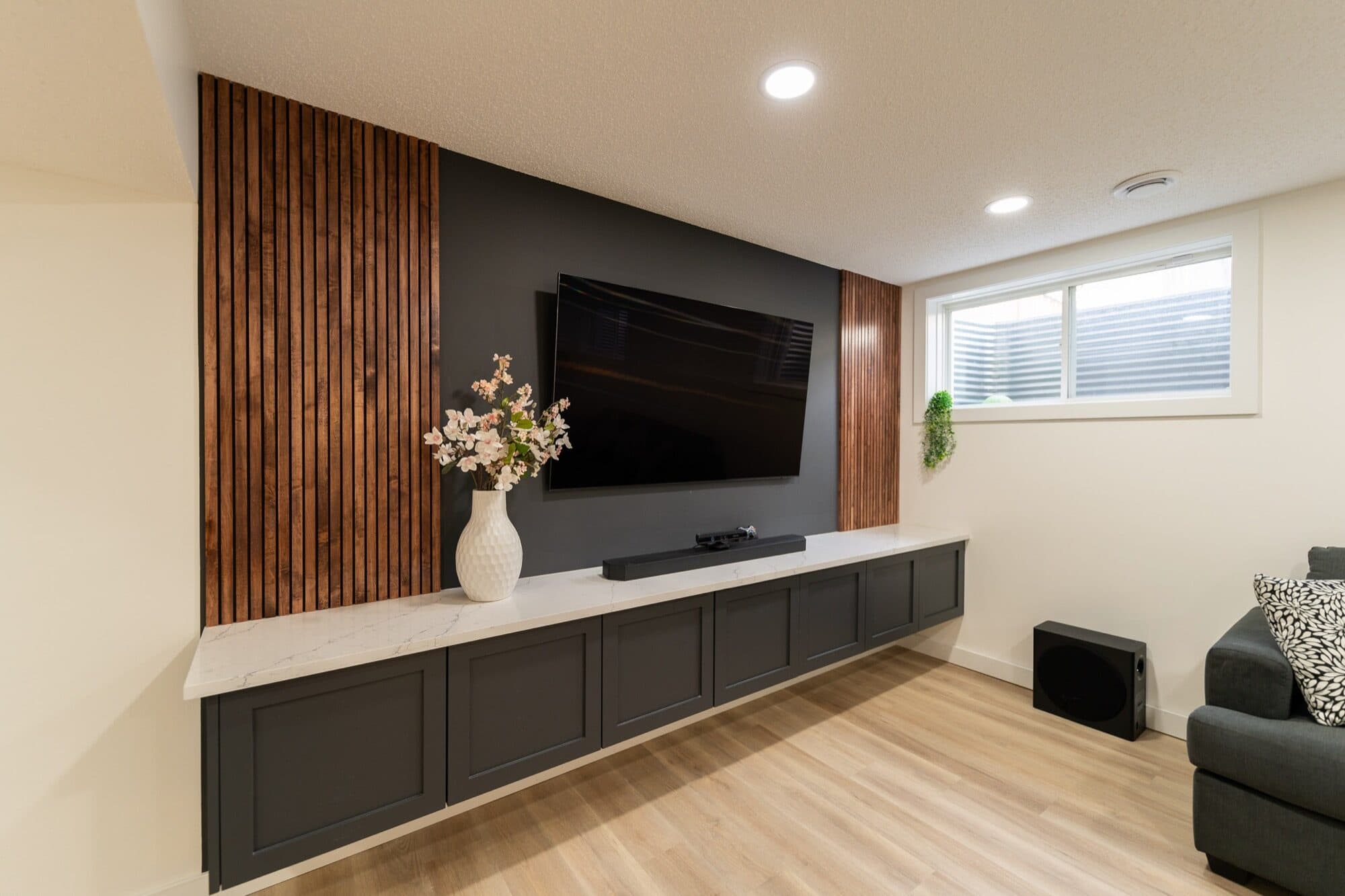 Basement rec room dark TV wall with wood slat panels and floating cabinet