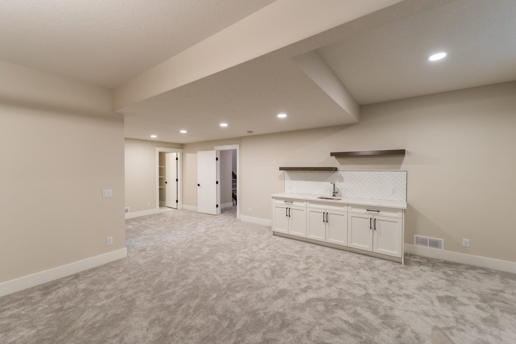 Basement wet bar with white shaker cabinets and herringbone tile backsplash
