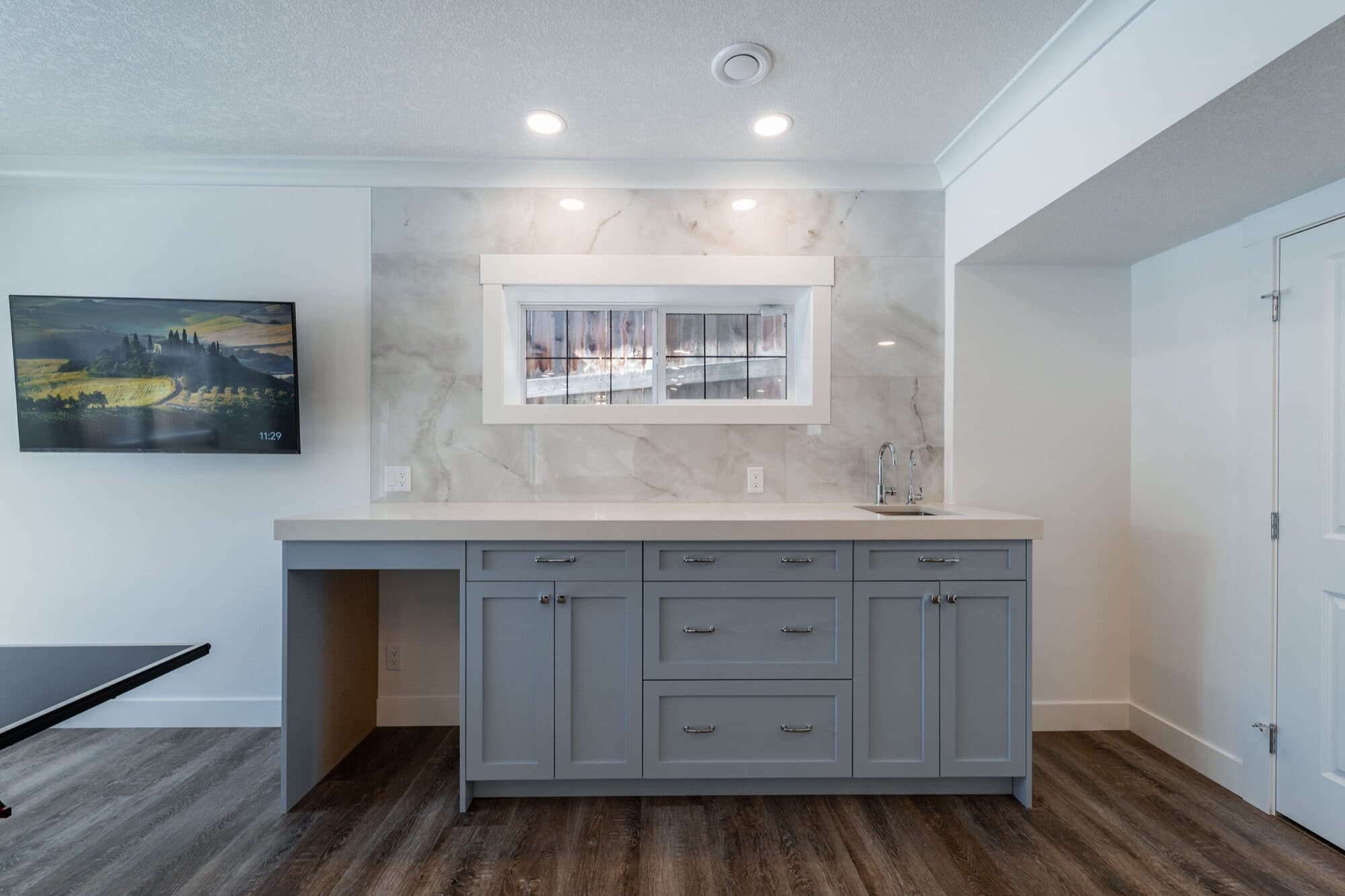 Basement bar with grey shaker cabinets and marble slab backsplash