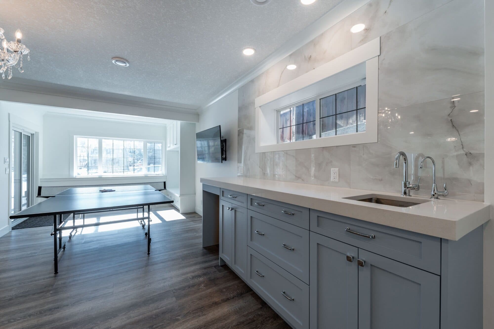 Basement bar with grey cabinets and marble backsplash, ping pong beyond