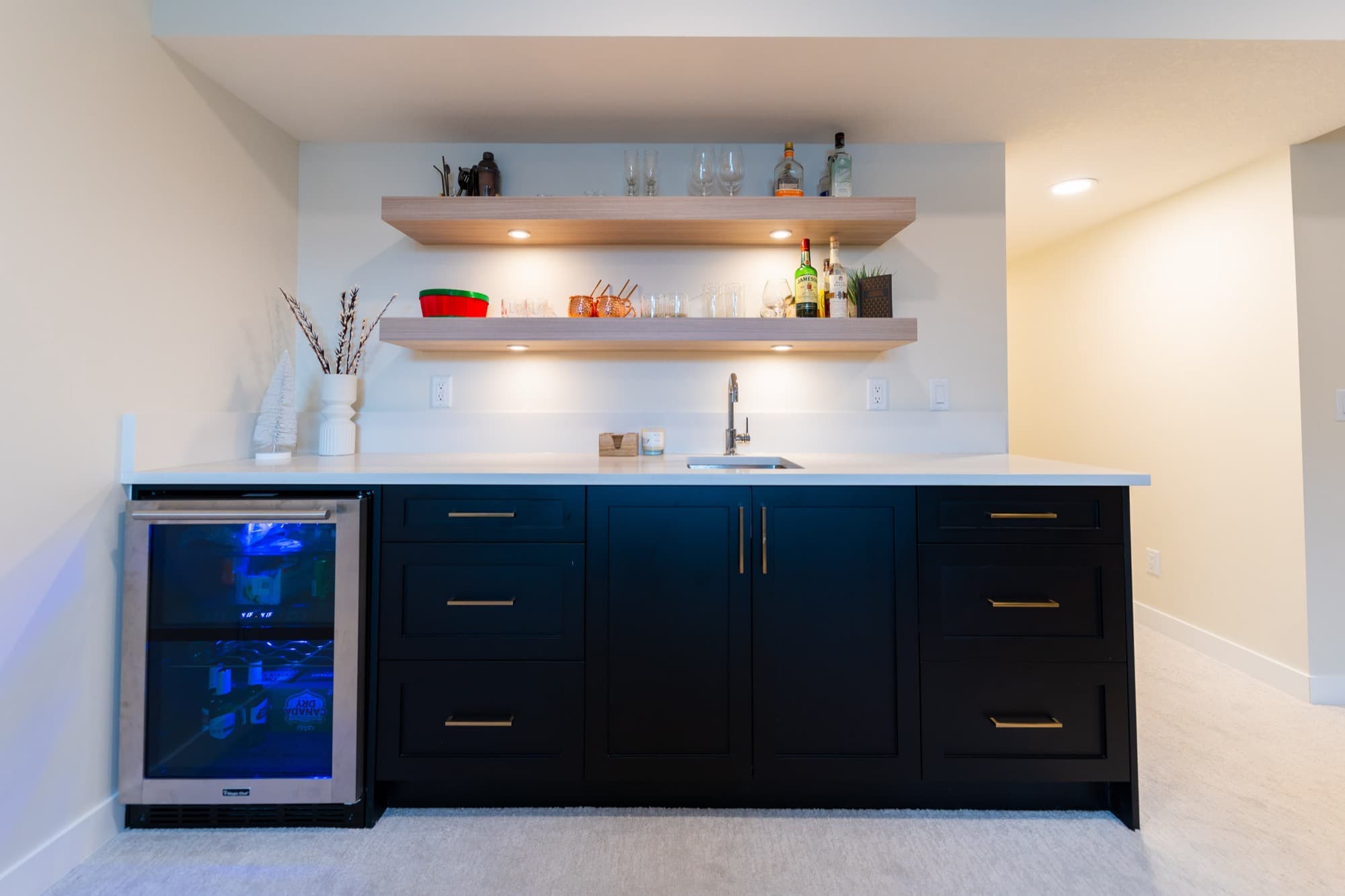 Basement wet bar with navy cabinets, wine fridge and floating shelves