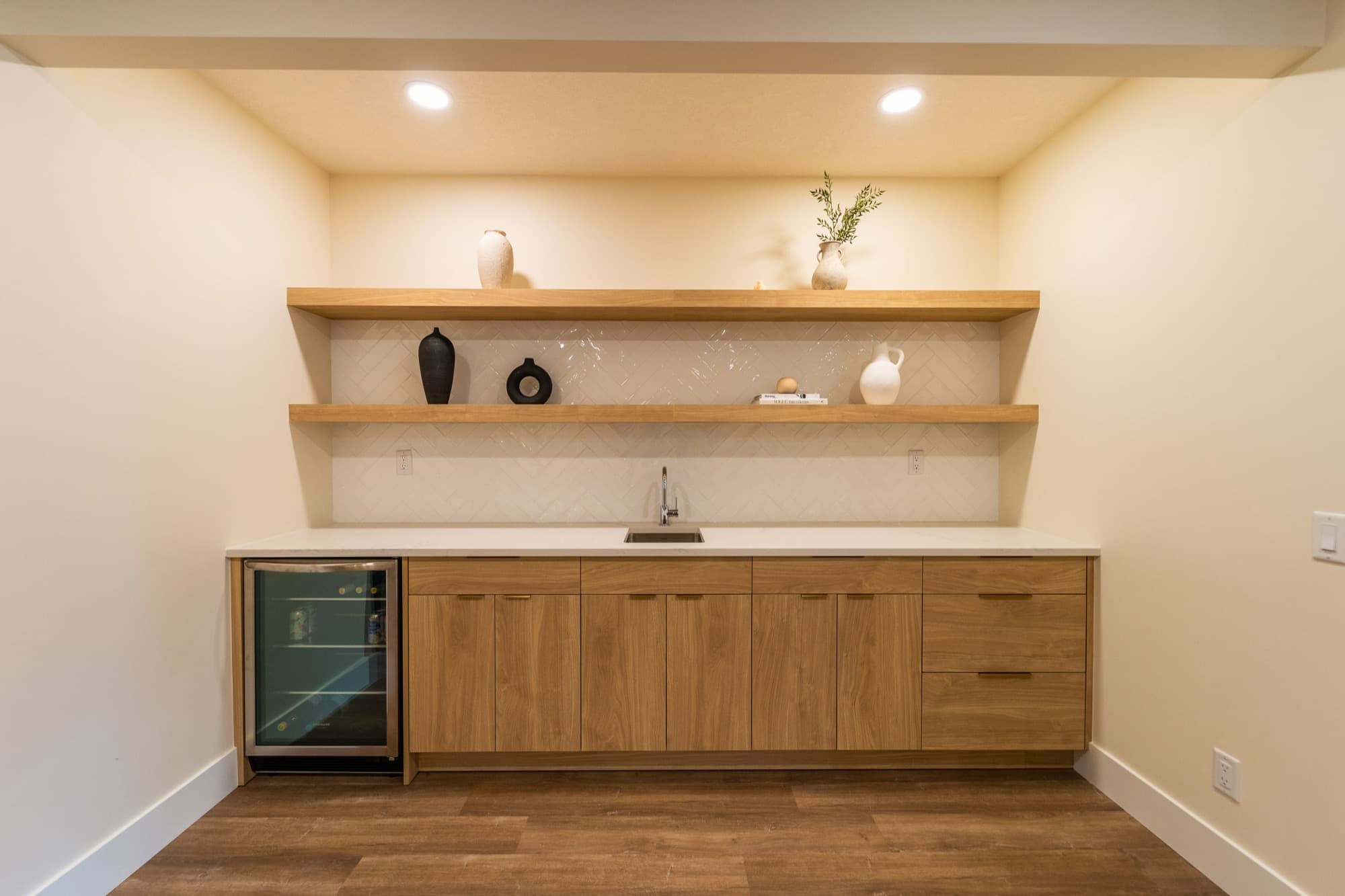 Basement bar with oak cabinets, herringbone tile and wine fridge