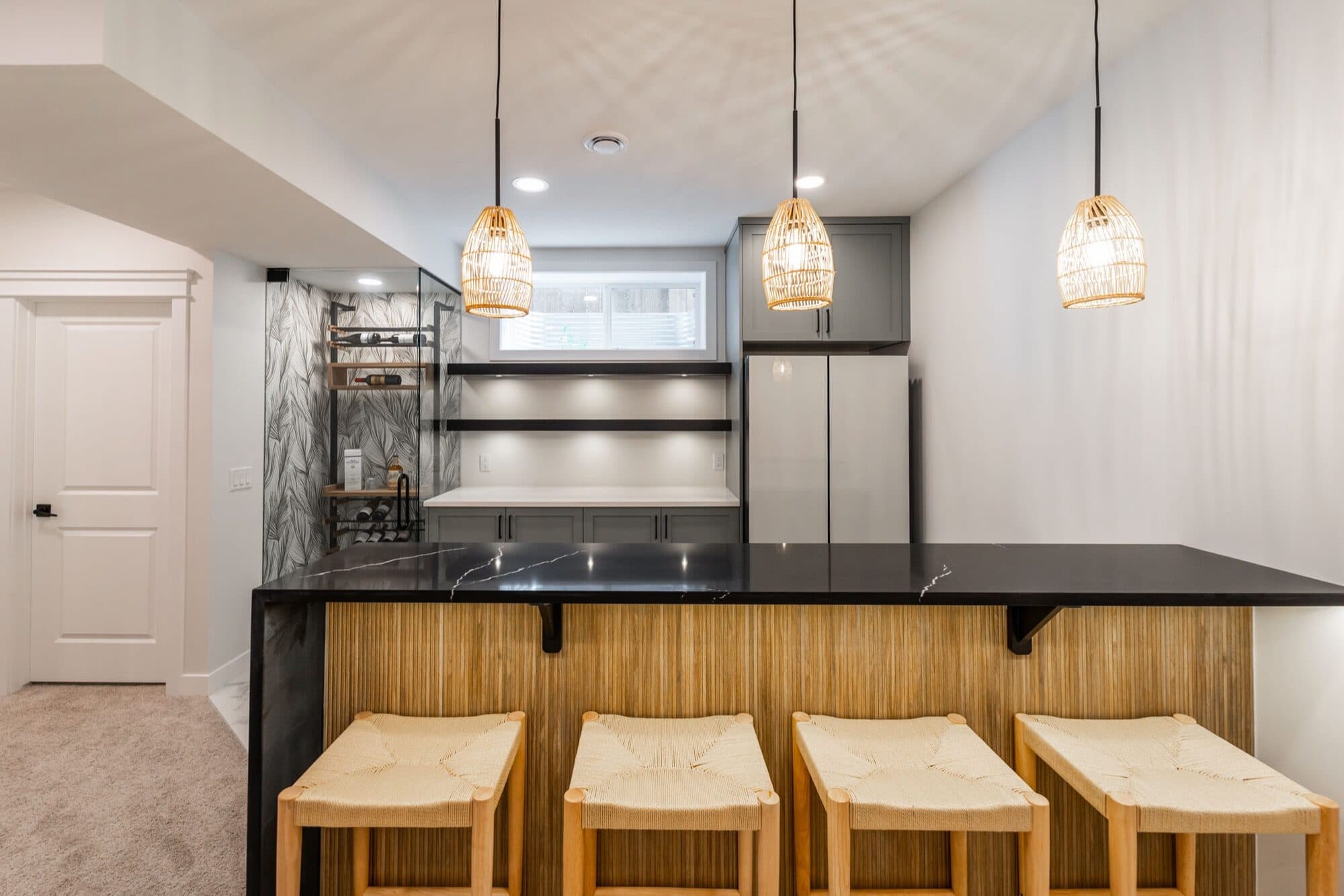 Basement bar with black marble counter, rattan stools and pendant lights