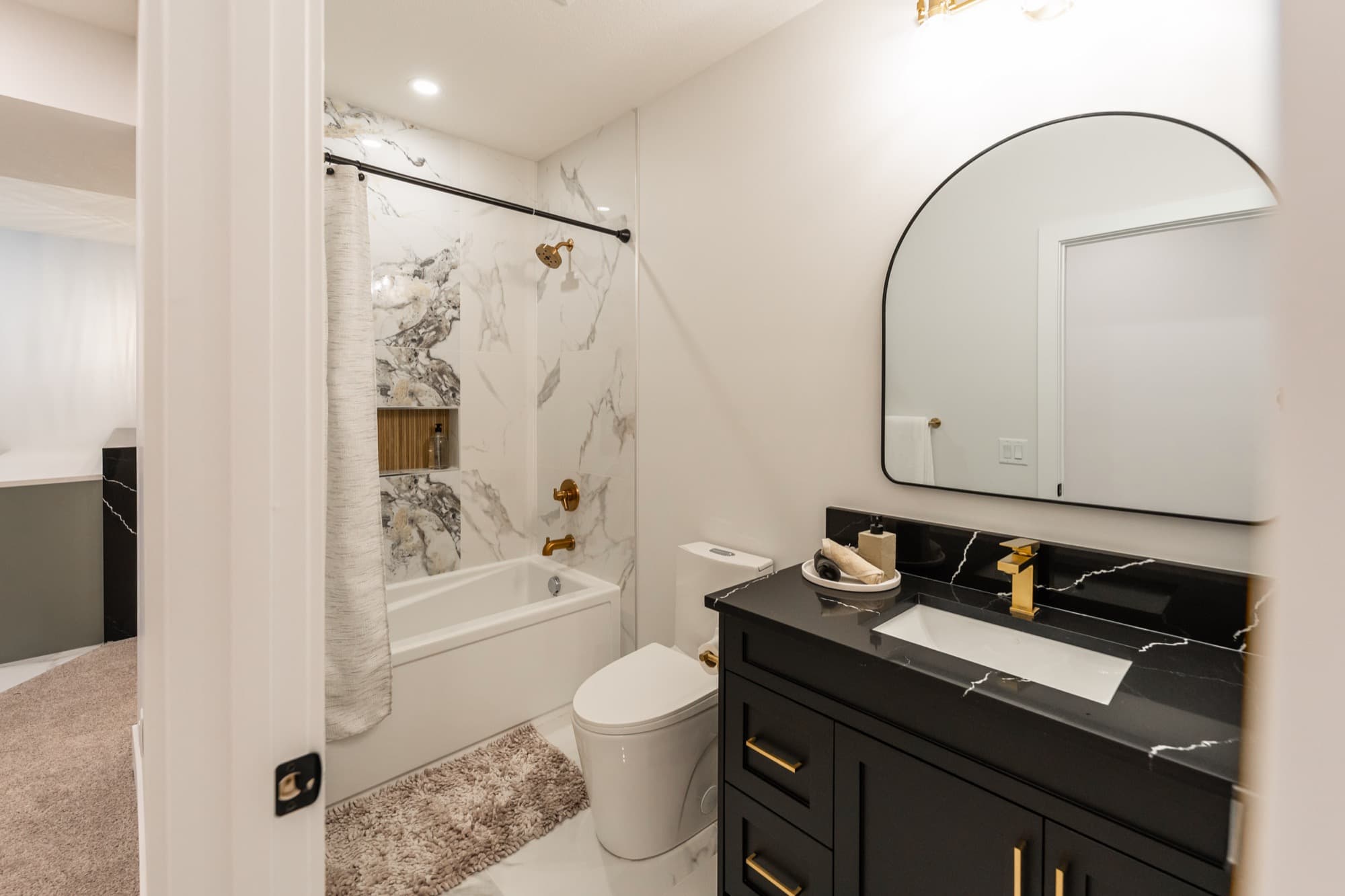 Basement bathroom with calacatta tub surround, gold hardware and black vanity