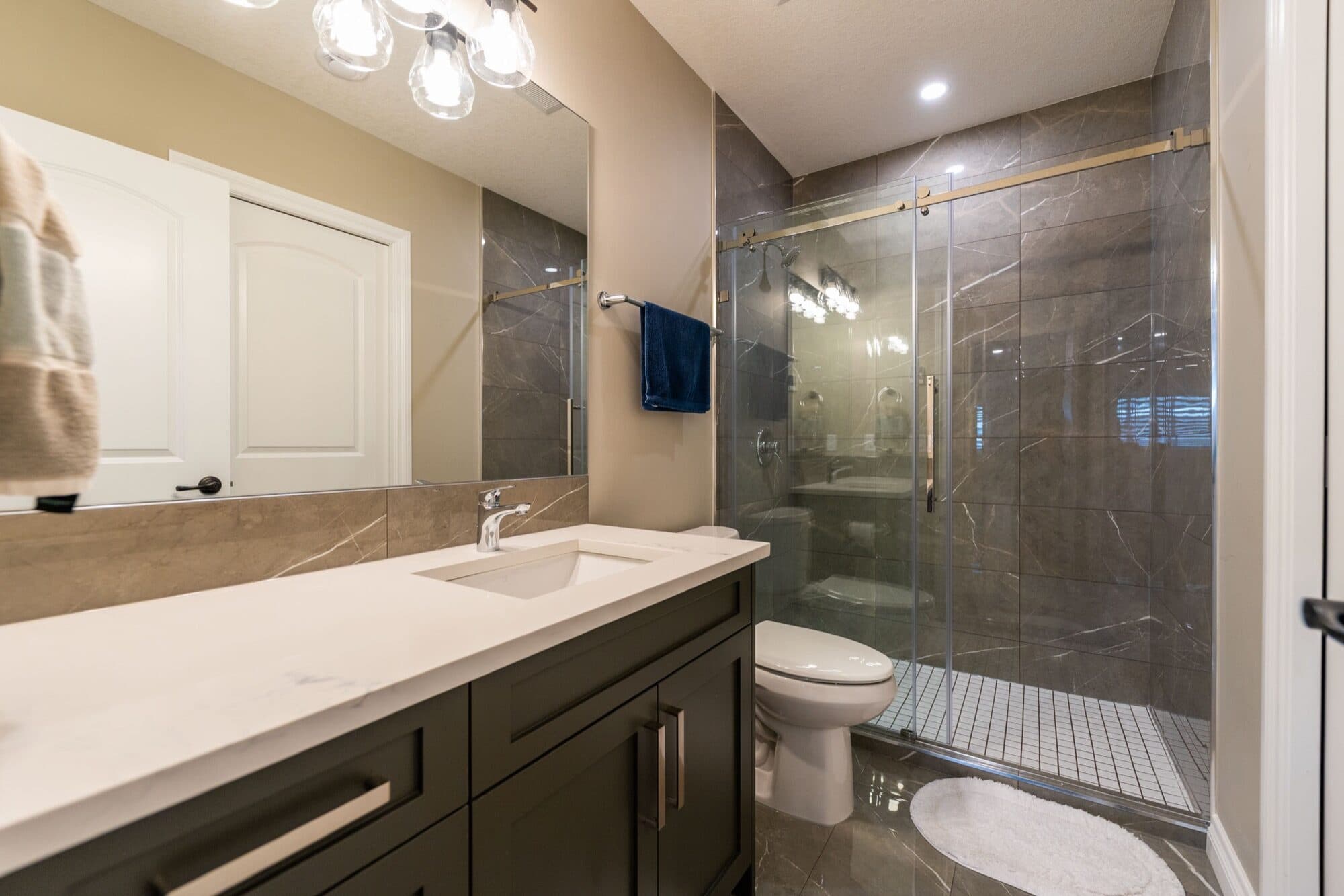 Basement bathroom with dark marble tile, glass shower and dark vanity