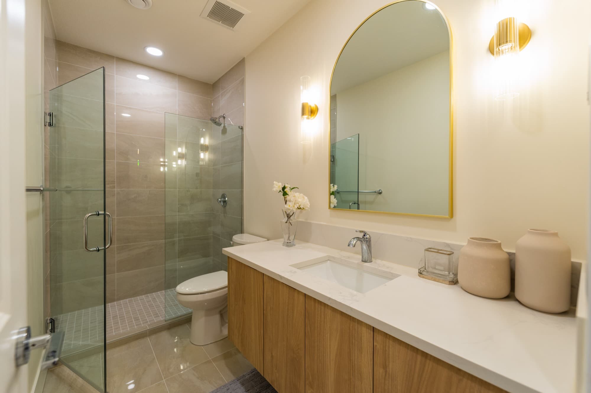 Basement bathroom with glass shower, gold hardware and arched mirror
