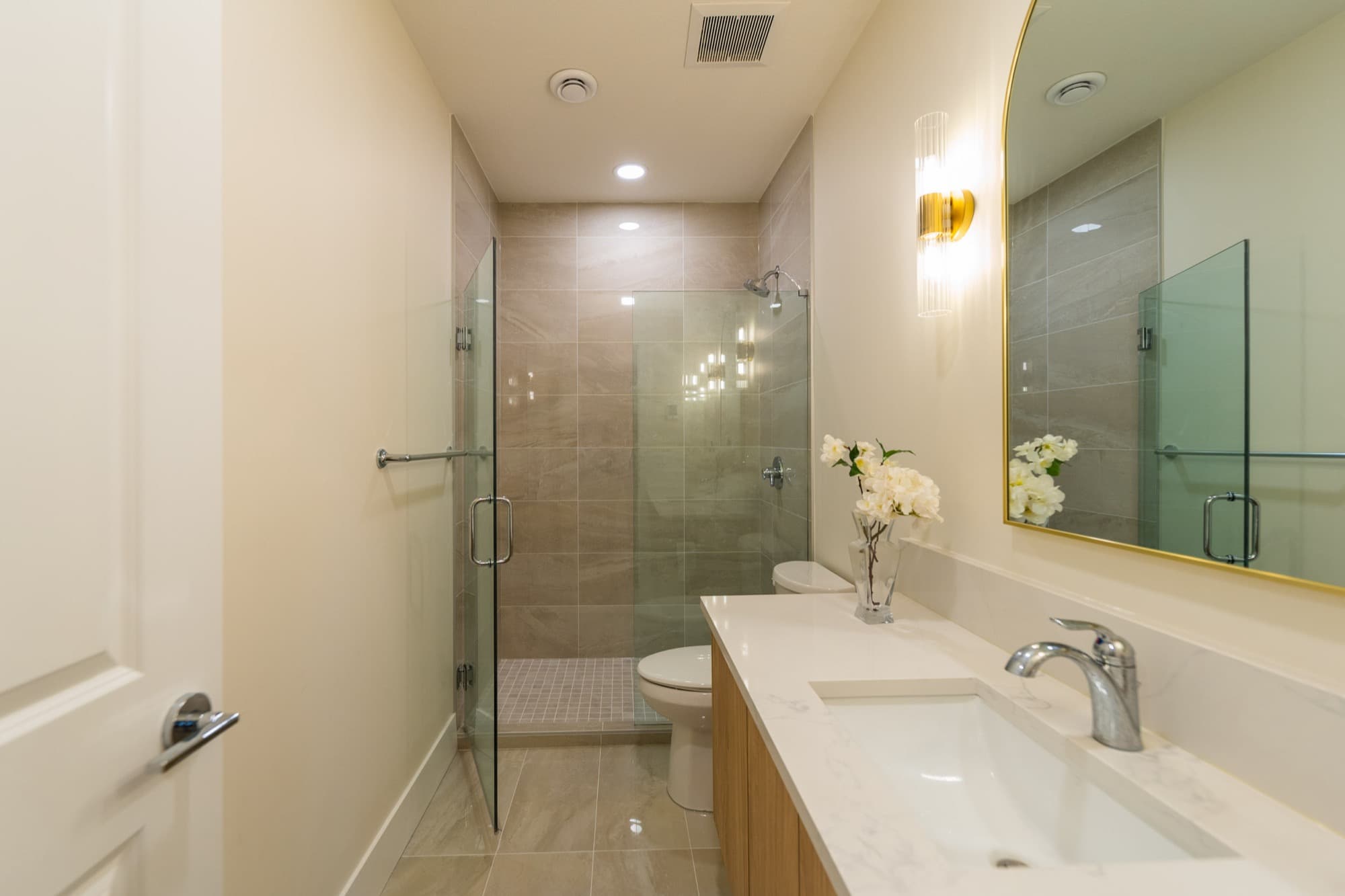 Basement bathroom with glass shower, taupe tile and gold arched mirror