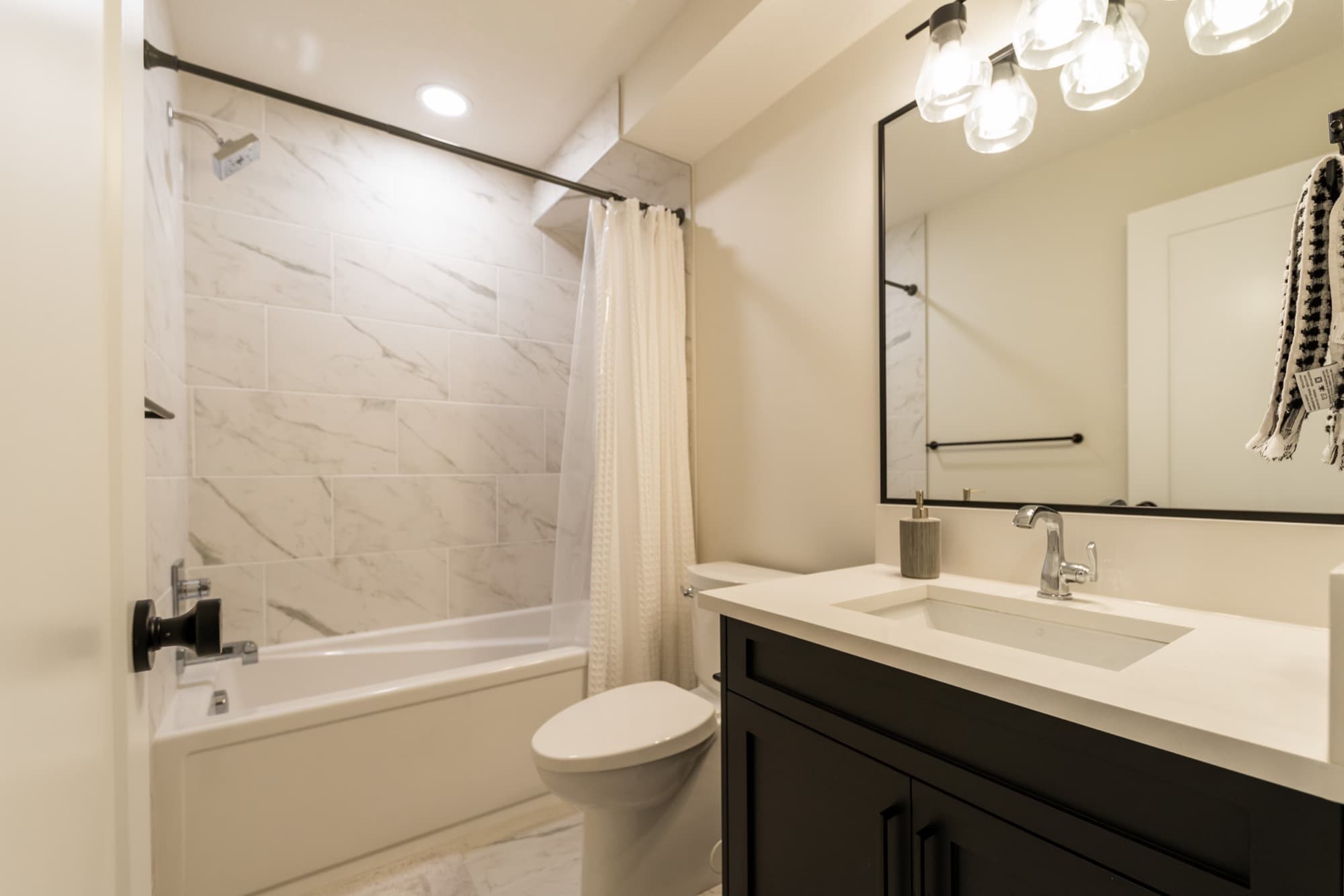 Basement bathroom with marble tile tub surround and black vanity fixtures