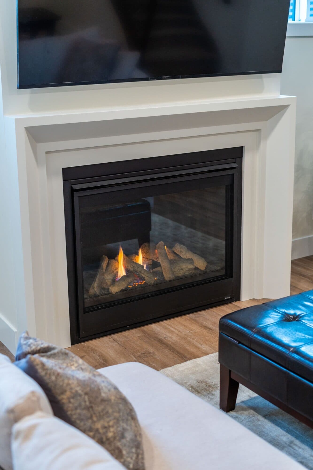 Basement gas fireplace close-up with lit flames and leather ottoman