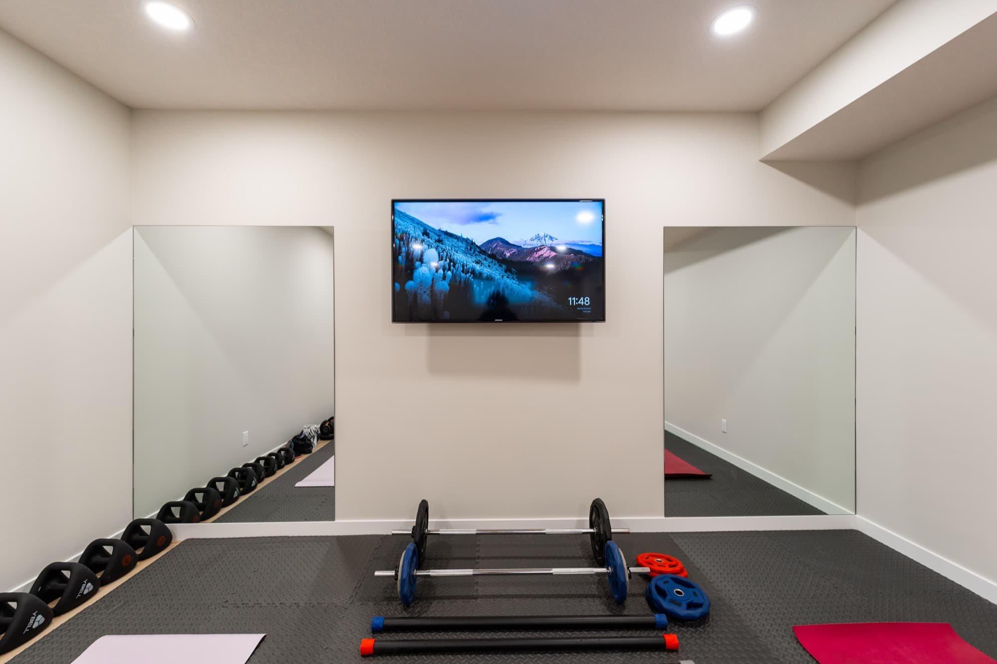 Basement gym with kettlebell rack, barbell, mirrors and wall-mounted TV