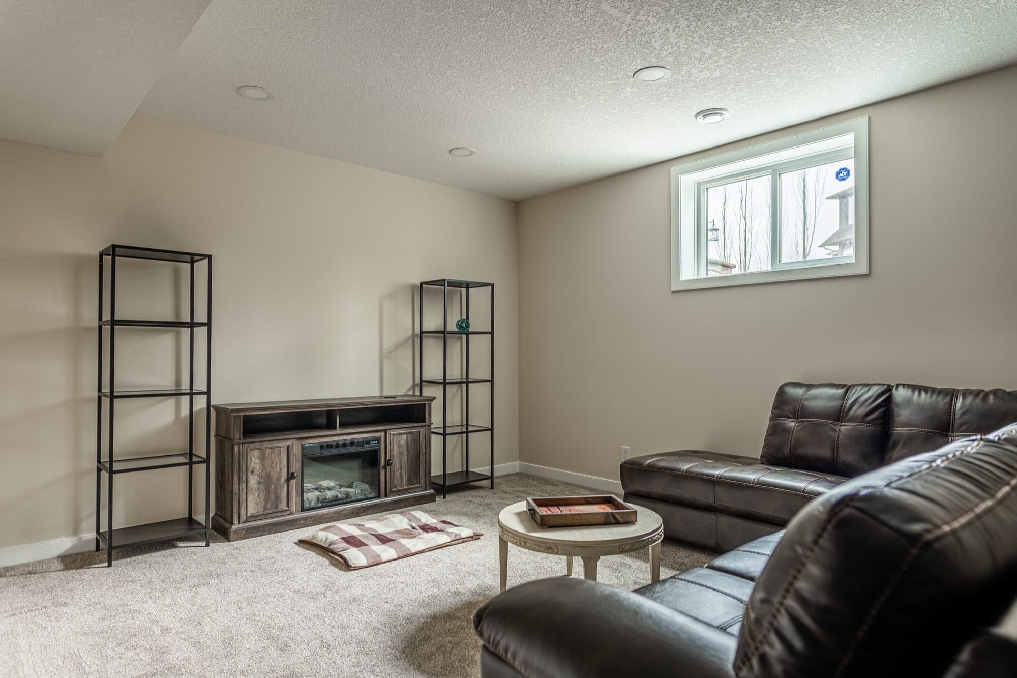 Basement rec room with leather sectional, electric fireplace and shelving