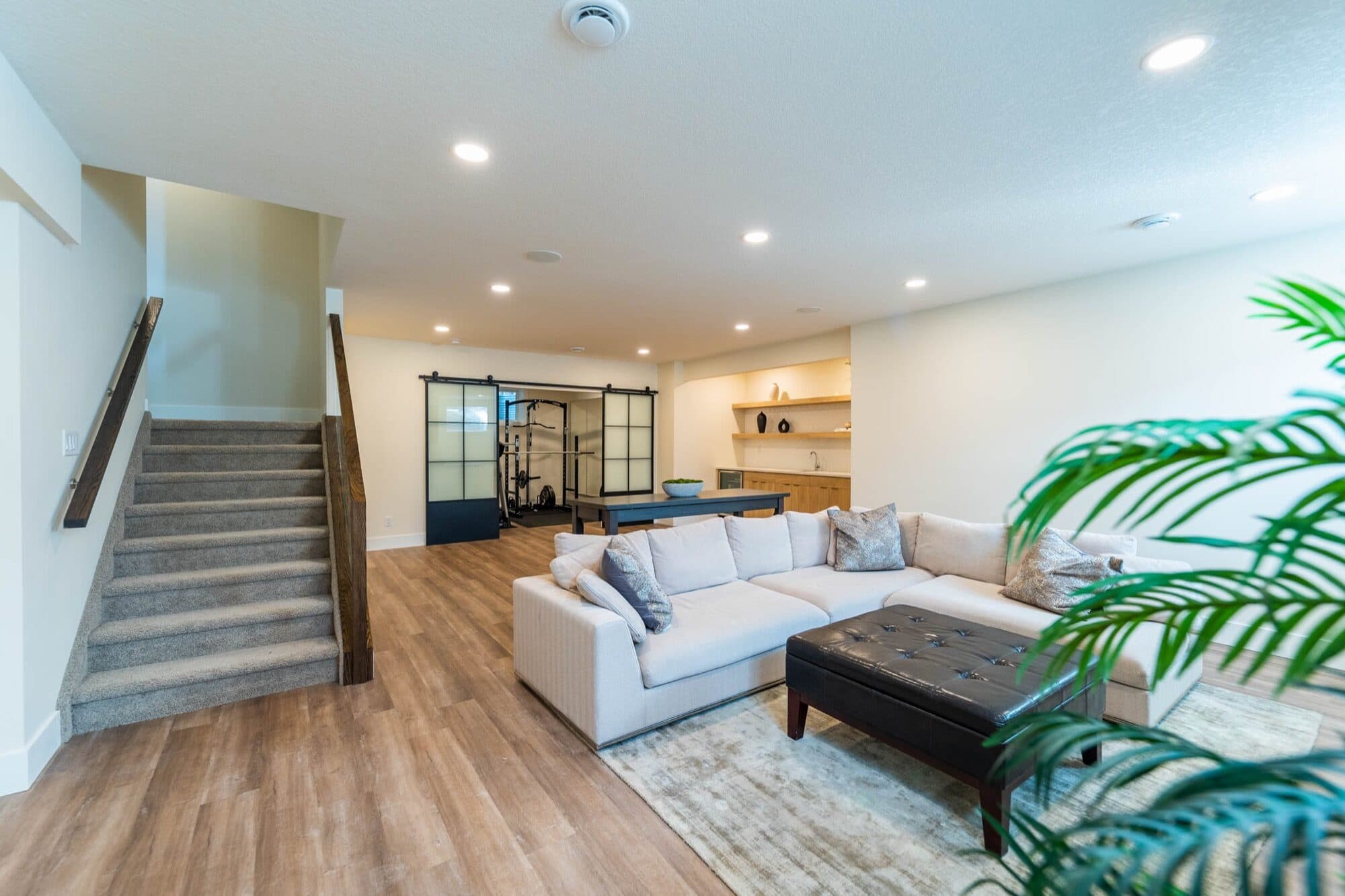 Basement open rec room with sofa, gym doors and bar, wide view