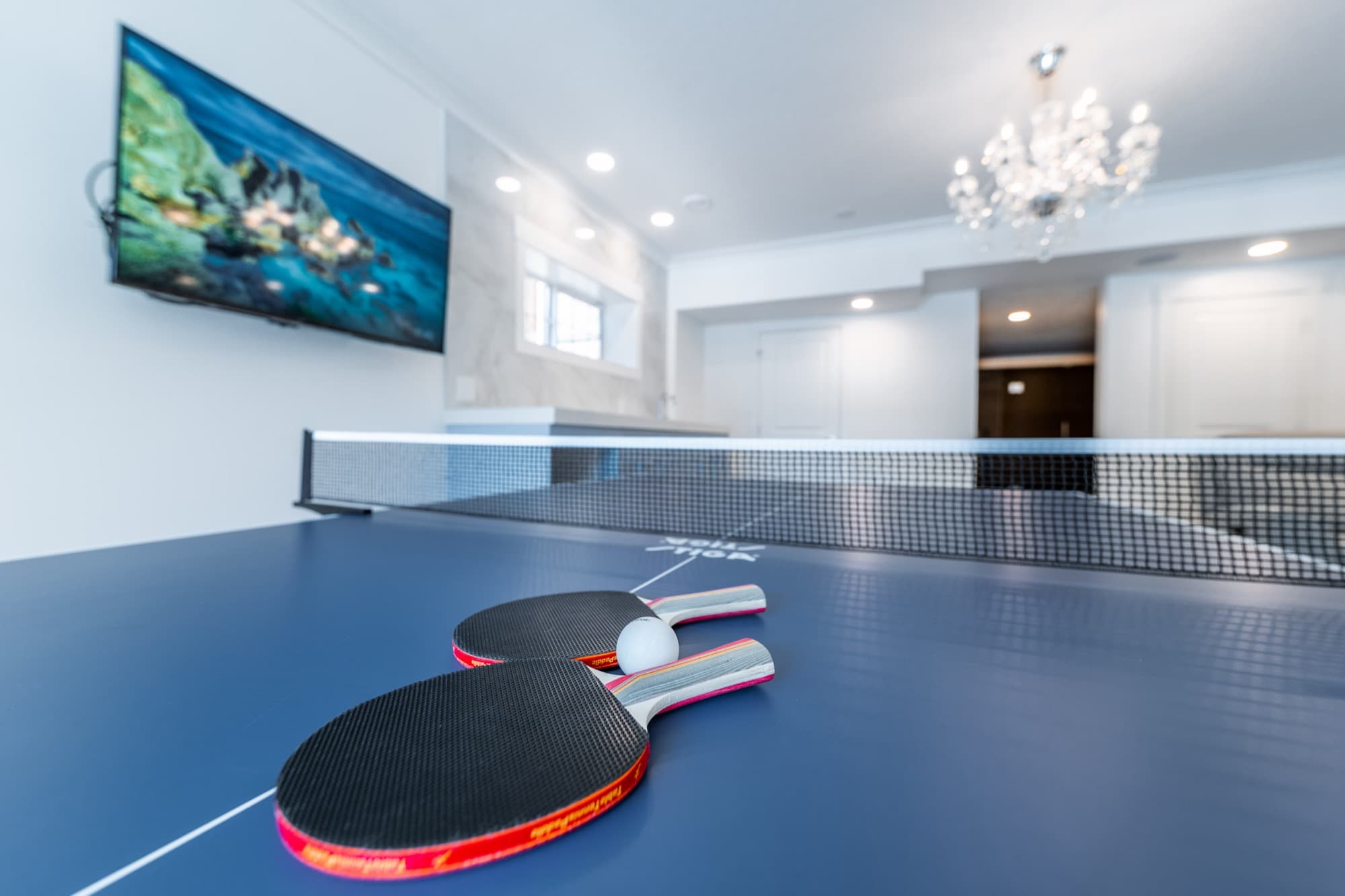 Basement rec room with ping pong table, chandelier, TV and marble bar