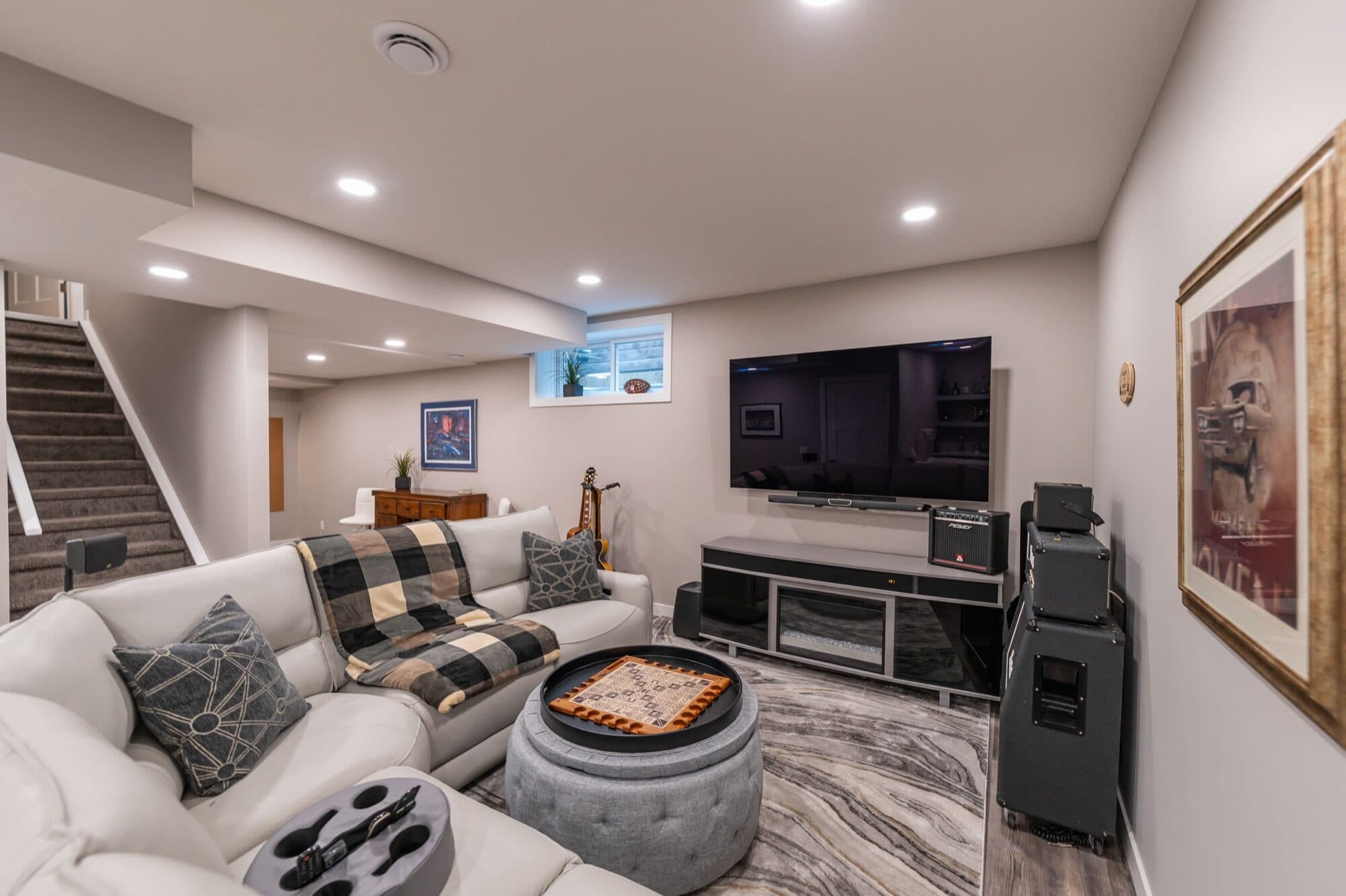 Basement rec room with white leather sectional, guitar and TV surround