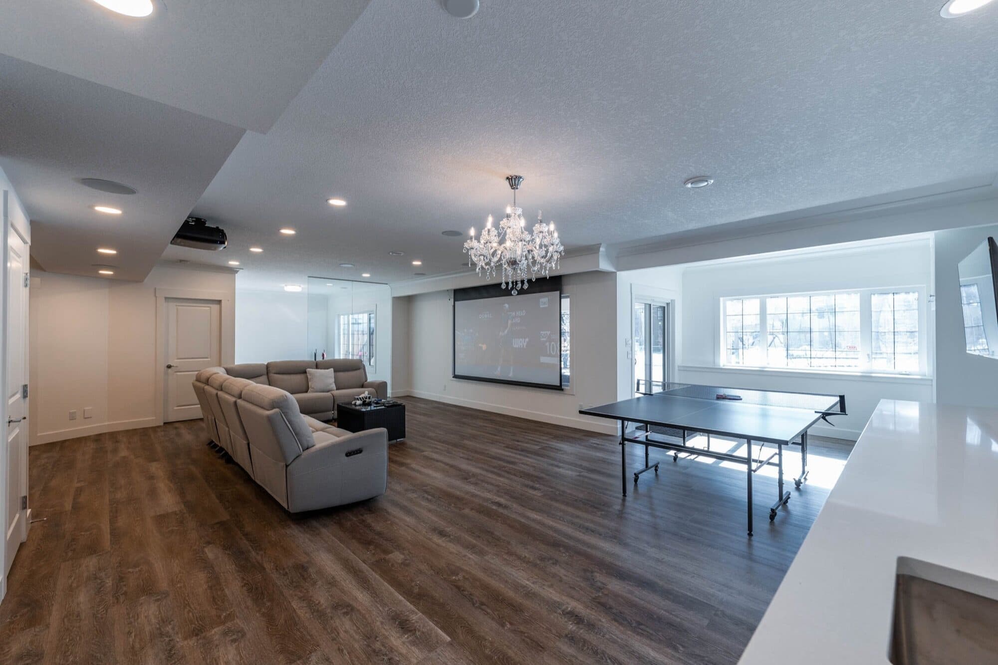 Basement rec room wide view with chandelier, projector screen and sofa