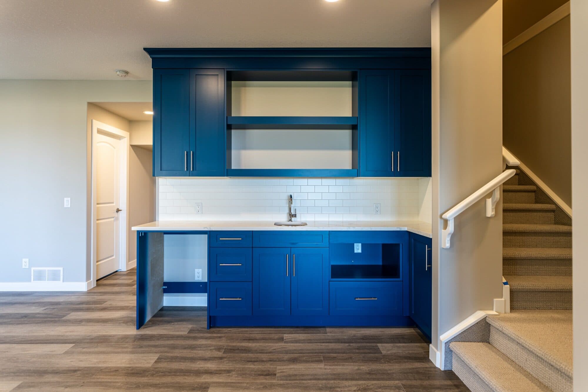 Basement with bold cobalt blue wet bar and staircase beside it