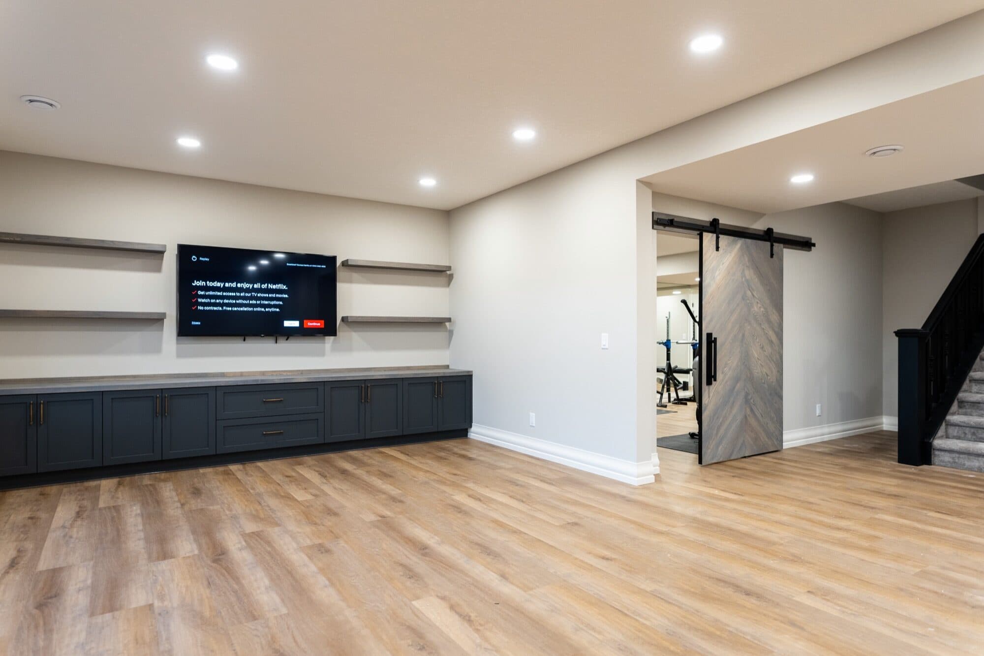 Basement rec room with dark built-in cabinet and barn door to gym