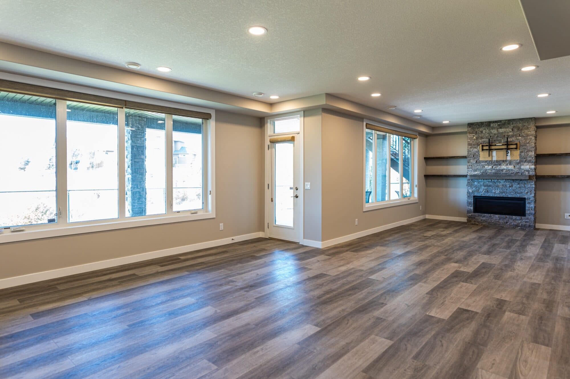 Wide-angle basement rec room with stone fireplace and wood-look flooring