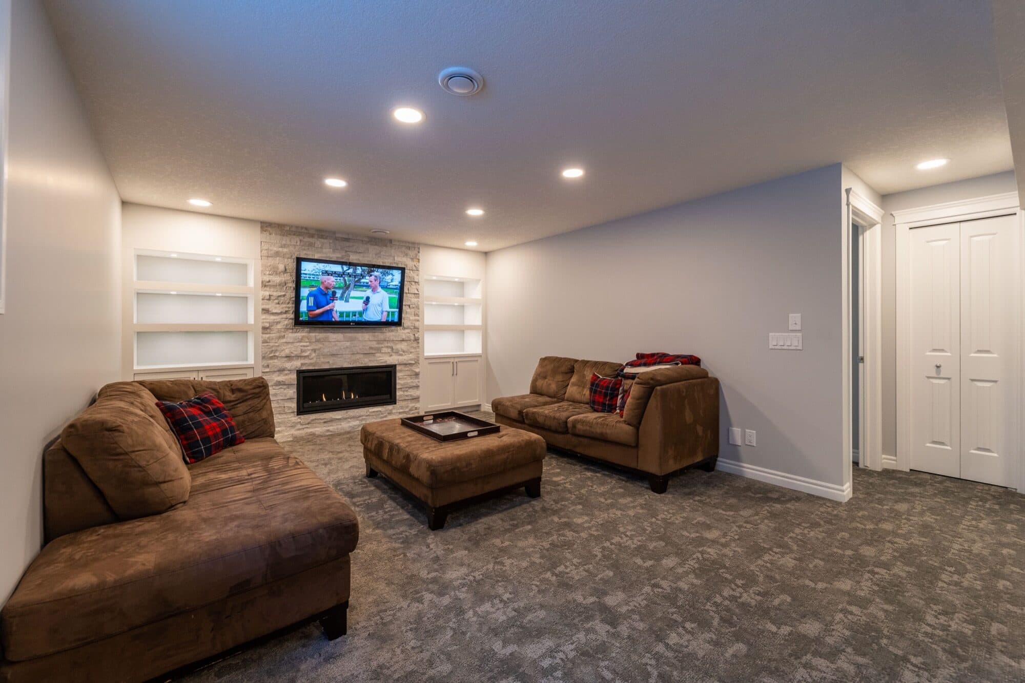 Cozy furnished basement rec room with stone fireplace and built-in shelves