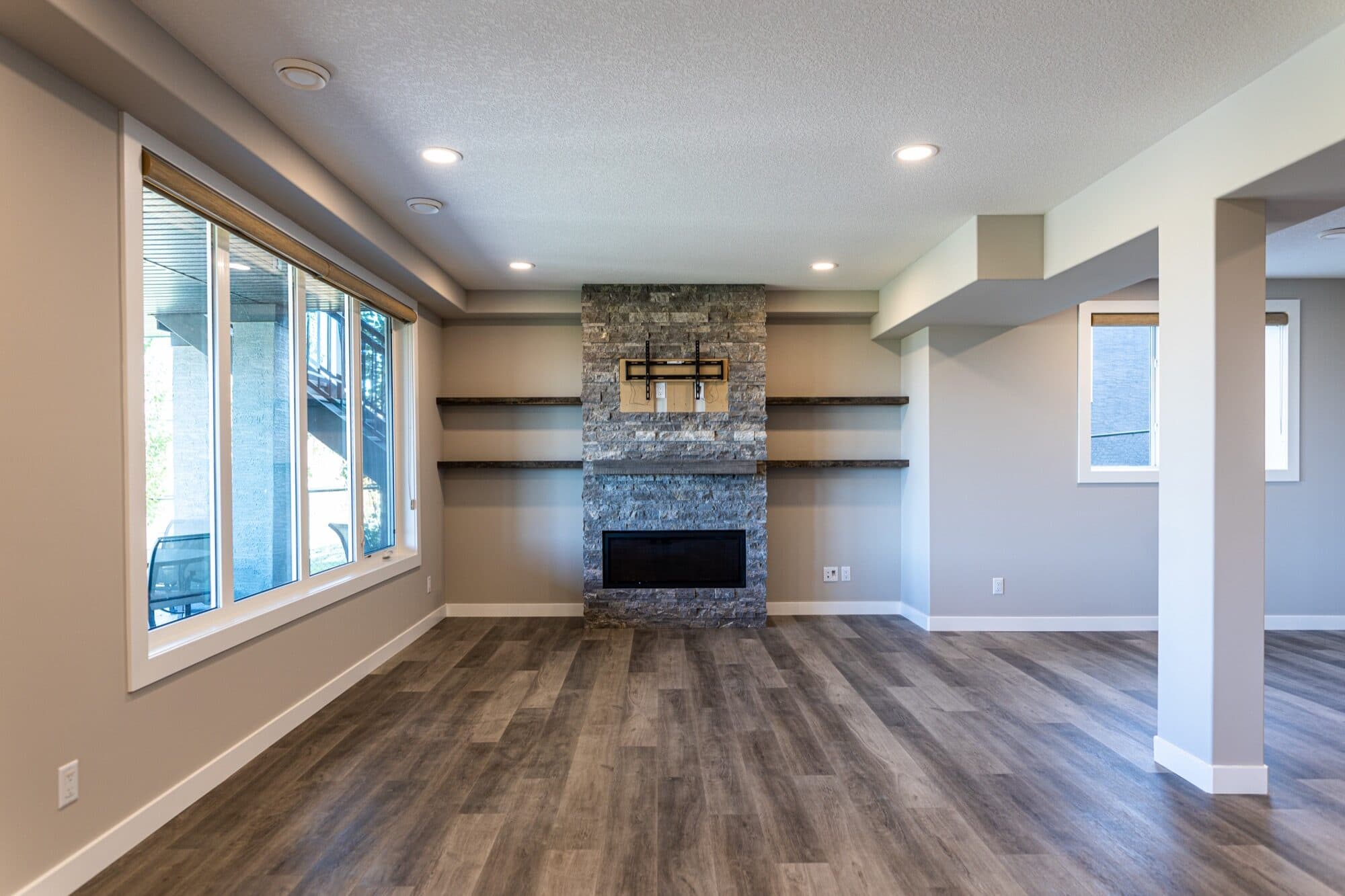 Open basement rec room with stone fireplace and floating shelves
